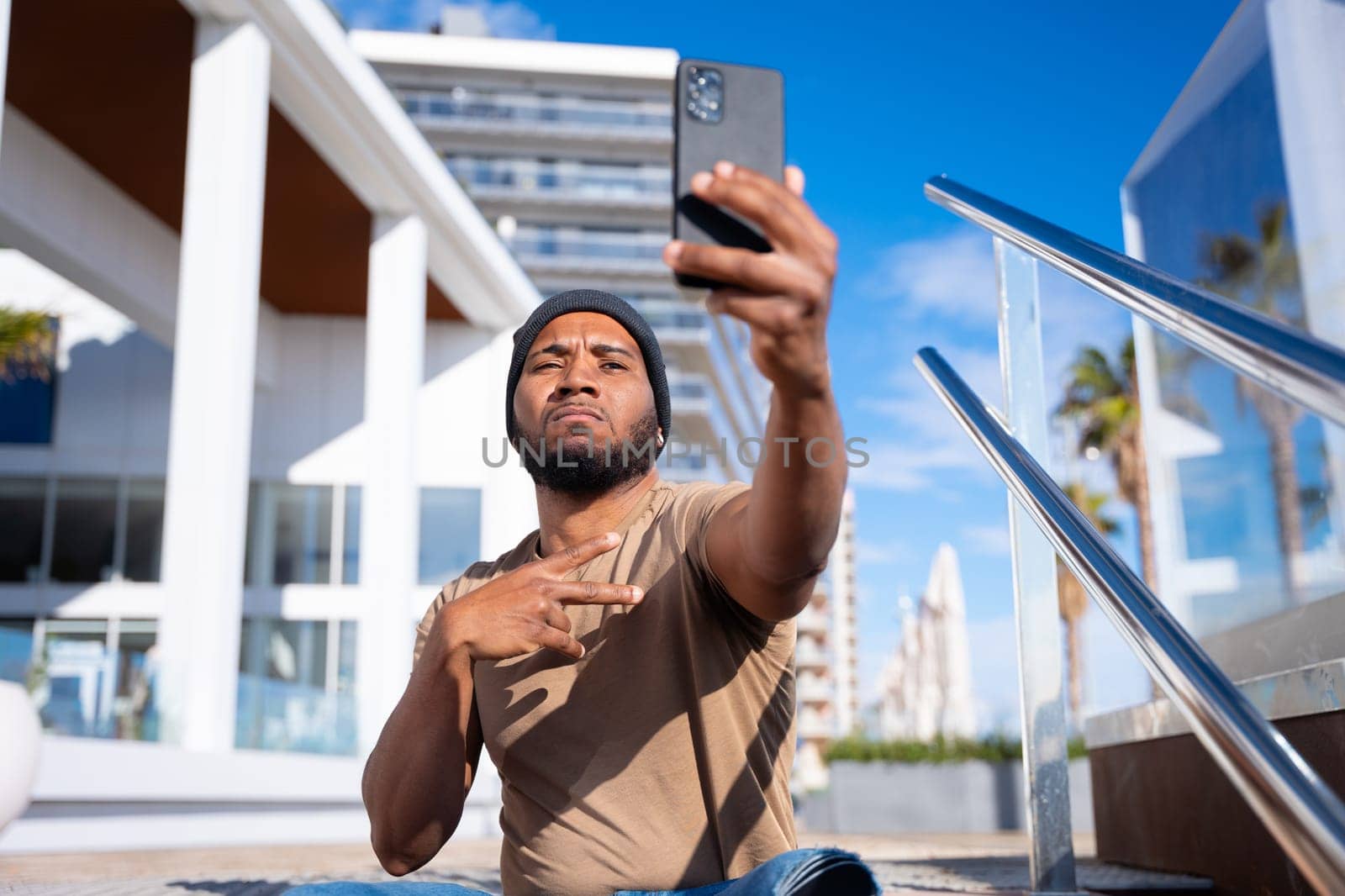 Self-portrait of a serious young hispanic man making the peace sign outdoors.