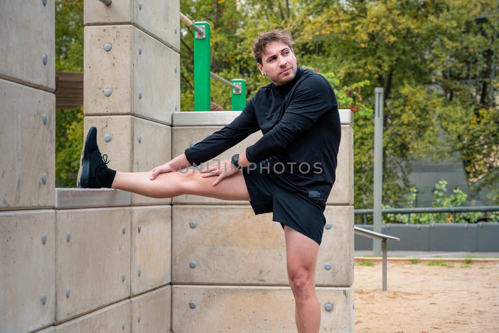 Young sportsman with concentrated sports watch stretching before training outdoors.