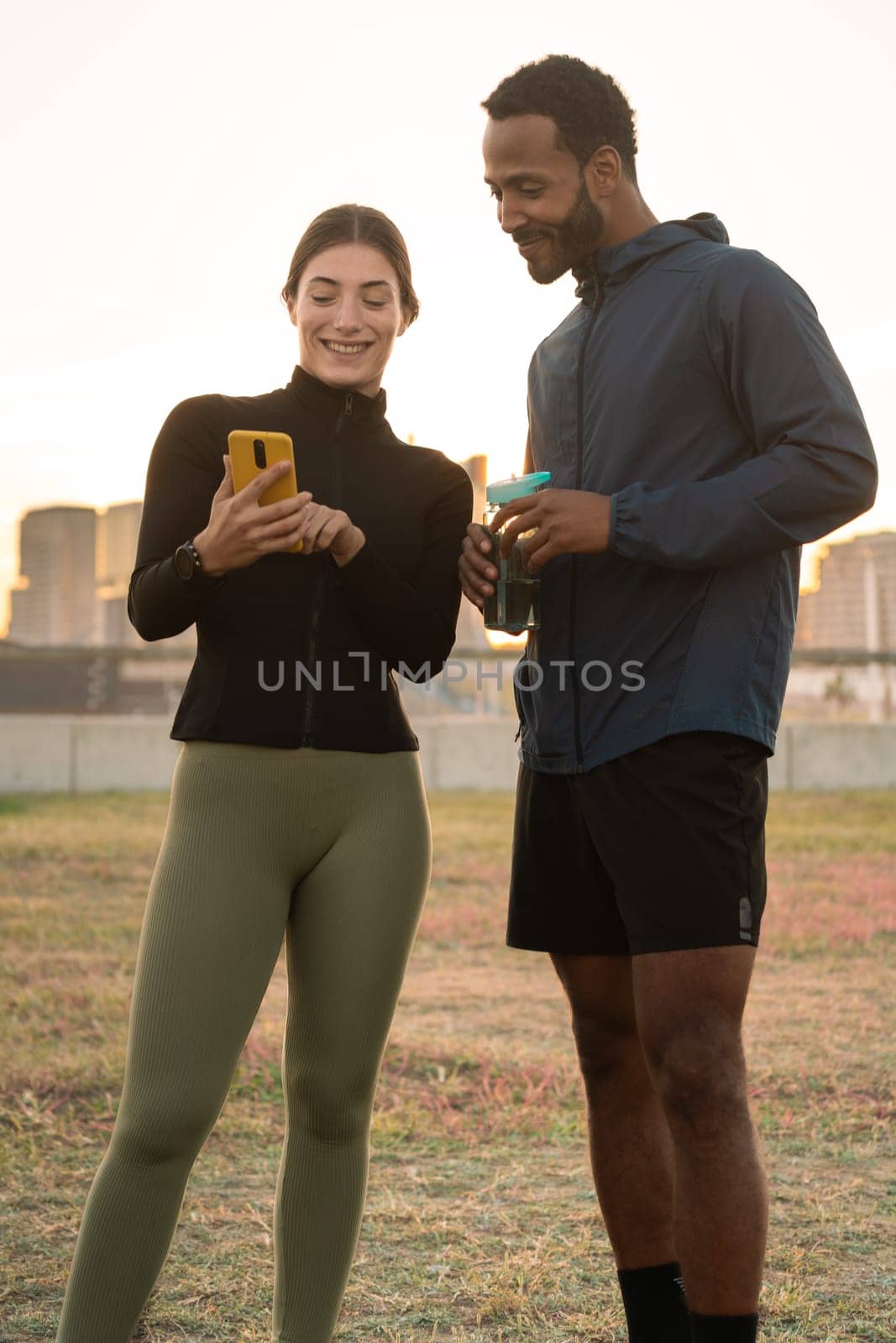 Vertical Photo of a young couple using a social media app on smartphone while exercising outdoors.