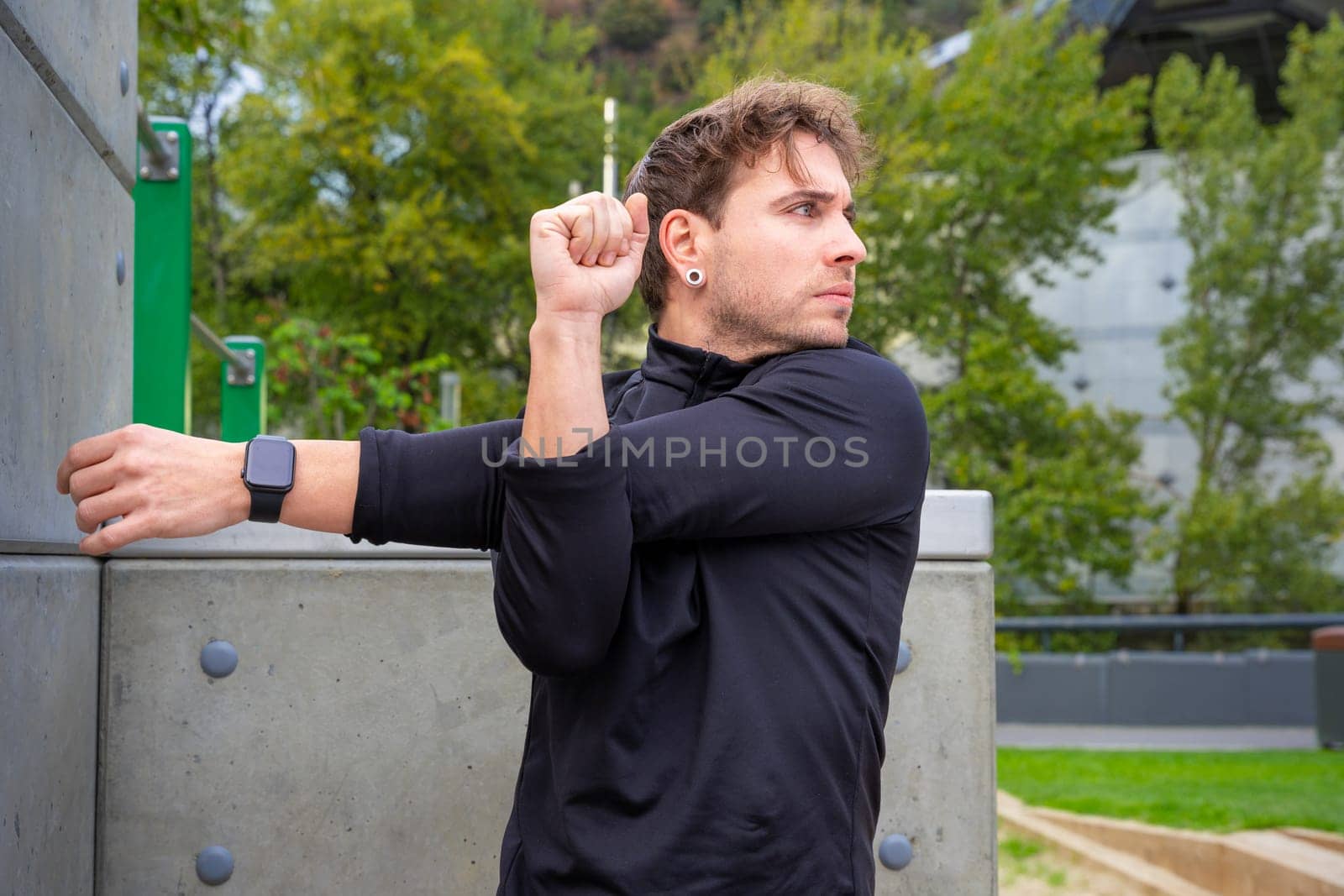 Young sporty man with sports watch stretching before training outdoors.