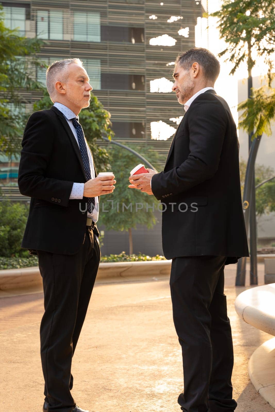 Portrait of two trusted business colleagues dressed in formal suit chatting together outside the workplace during work meeting.