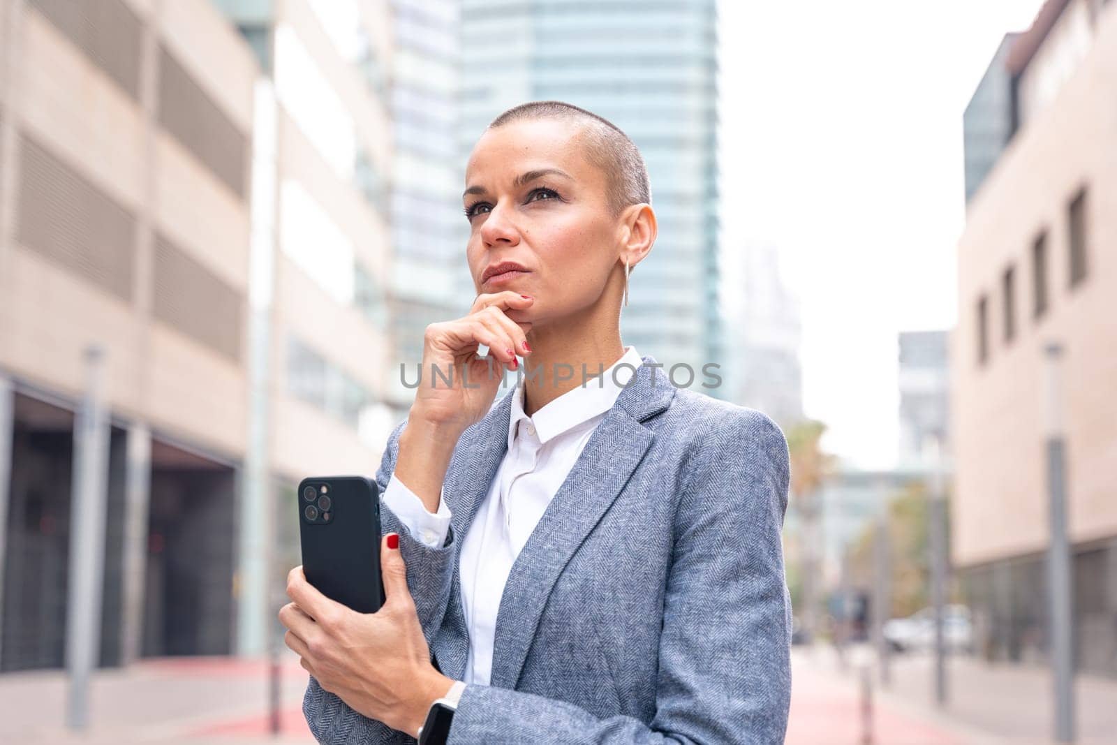 Thoughtful businesswoman with results of businesswoman walking down the street outside office building, a mature boss holds a phone in her hands, writes messages and reads news online, using an app.
