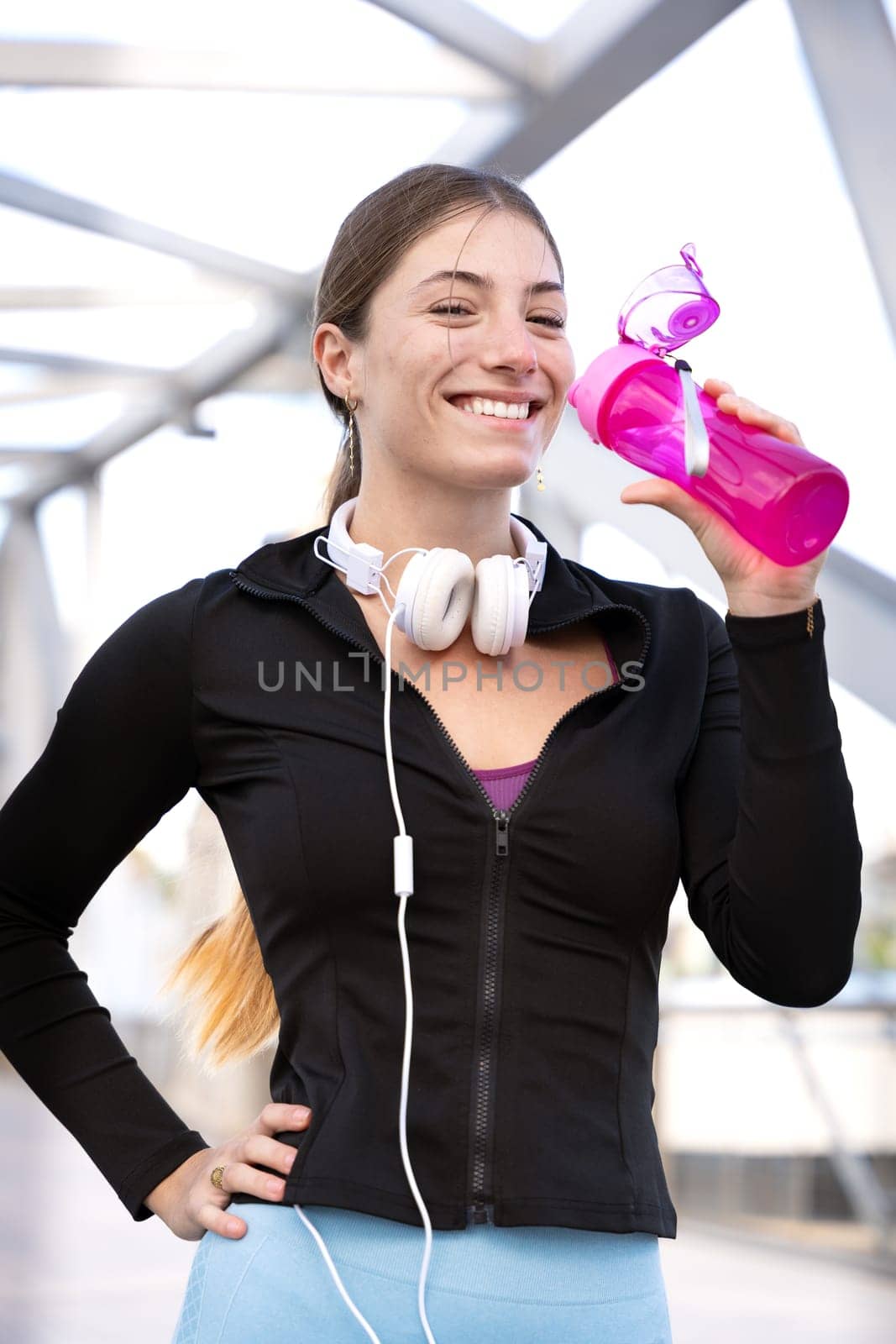 athletic woman with headphones smiling drinking water while exercising