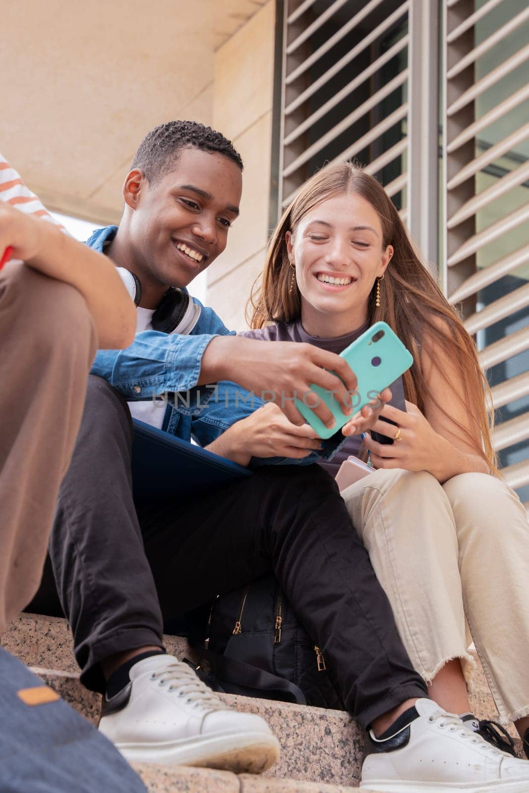 smiling multiracial students sitting outdoors using cell phone to chat online. University life concept