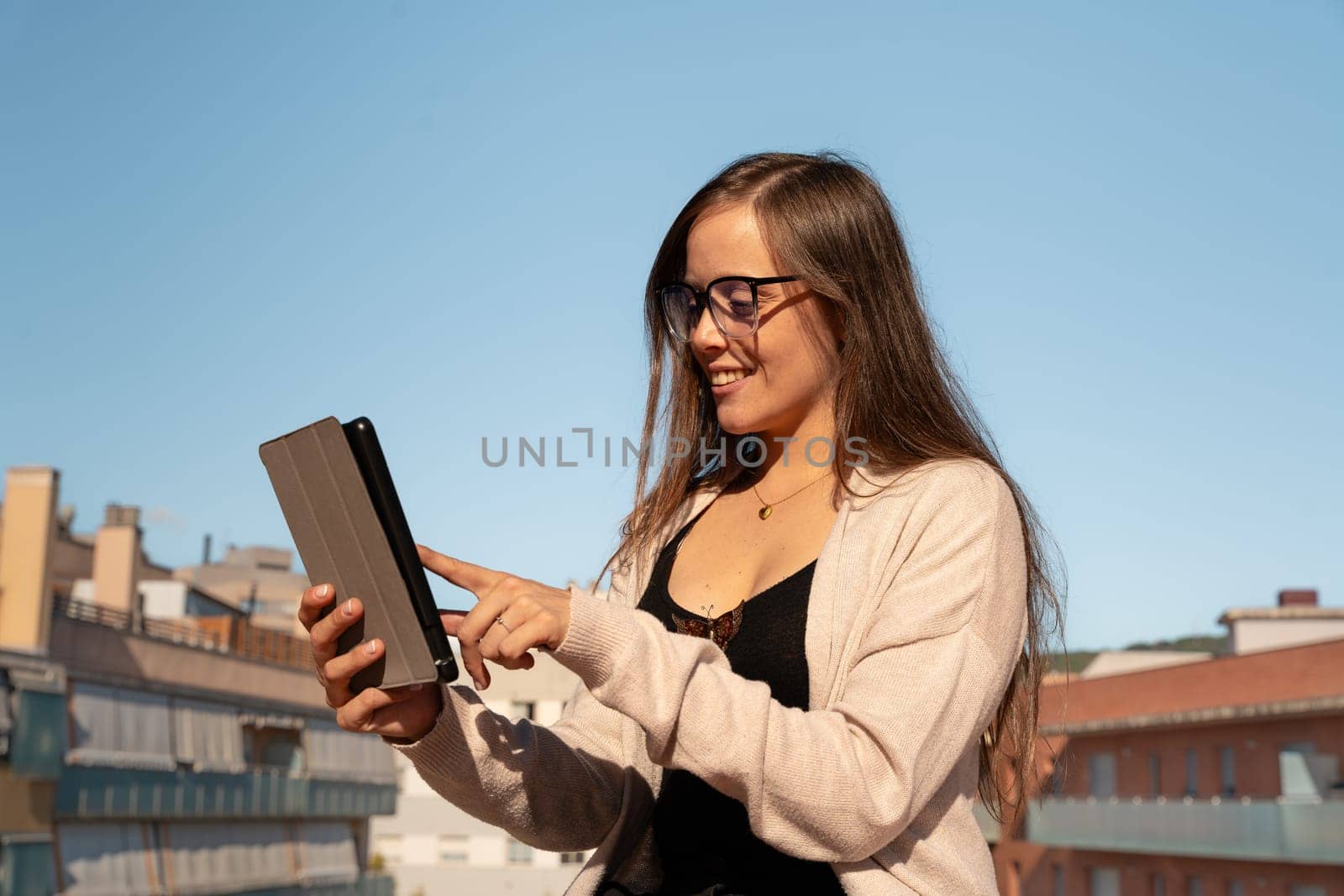 Beautiful young adult caucasian woman with glasses typing on tablet pc happy