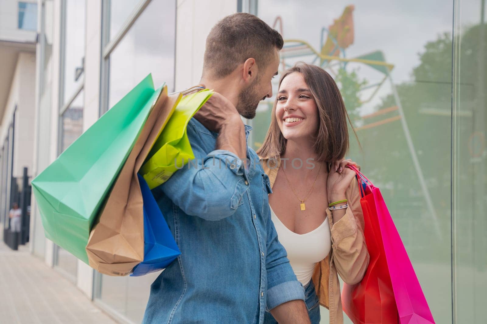 happy young adults in the shopping center. portrait of a laughing caucasian man and woman carrying shopping bags