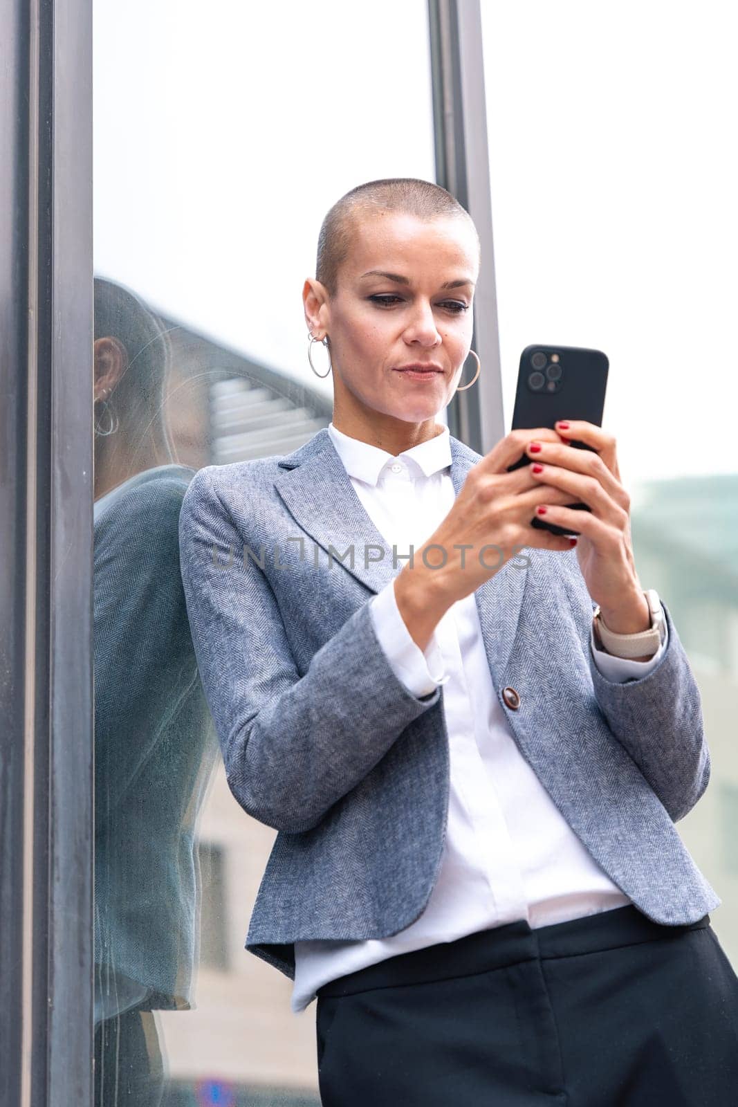 Satisfied with the results, the businesswoman walking on the street outside the office building, a mature boss holds a phone in her hands, writes messages and reads news online, using an app.