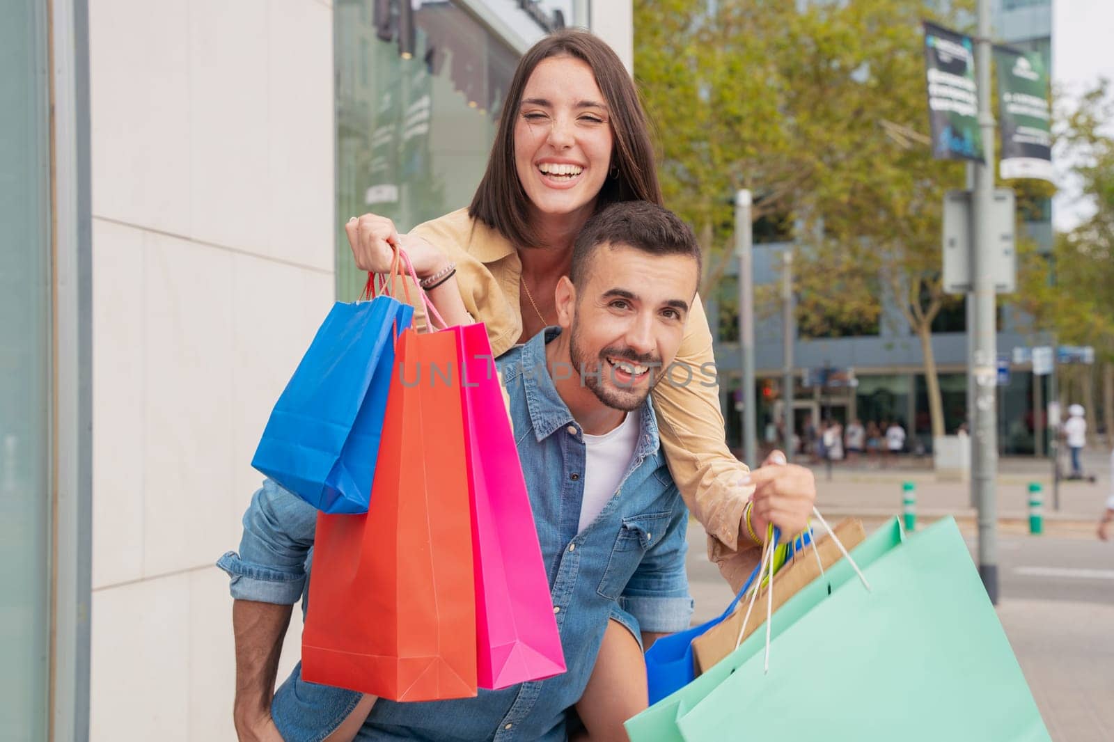 Happy caucasian man carrying his girlfriend on his back having fun together carrying shopping bags Concept of excitement, weekend and family.