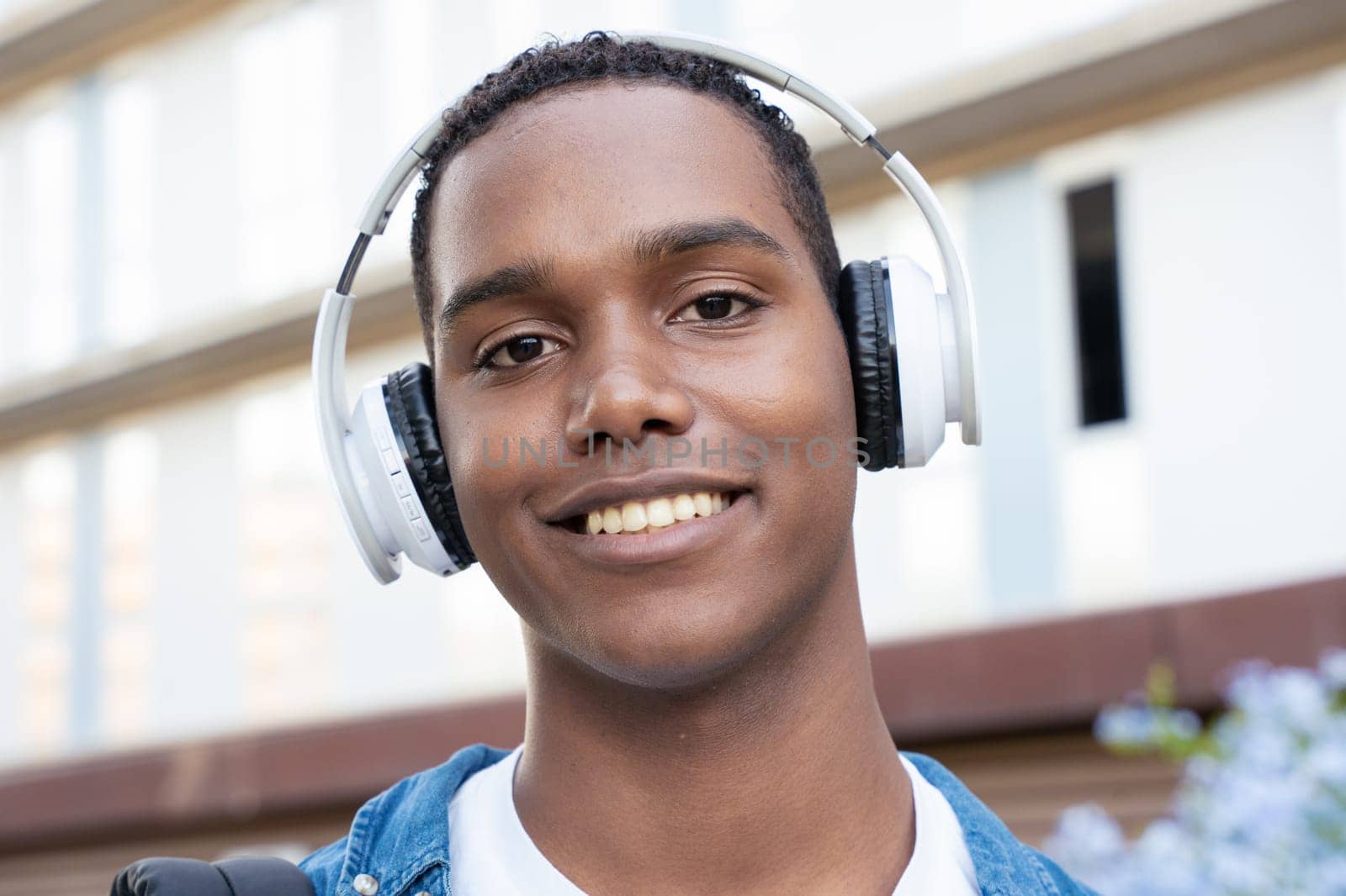 Young black man student standing outdoors at university with headphones.College life concept