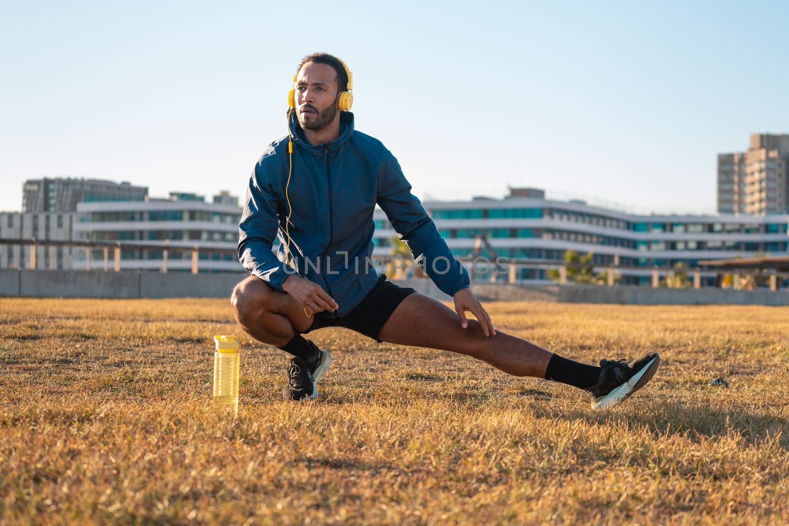 Young latin sportsman with sports headphones doing stretches with water bottle on the floor.