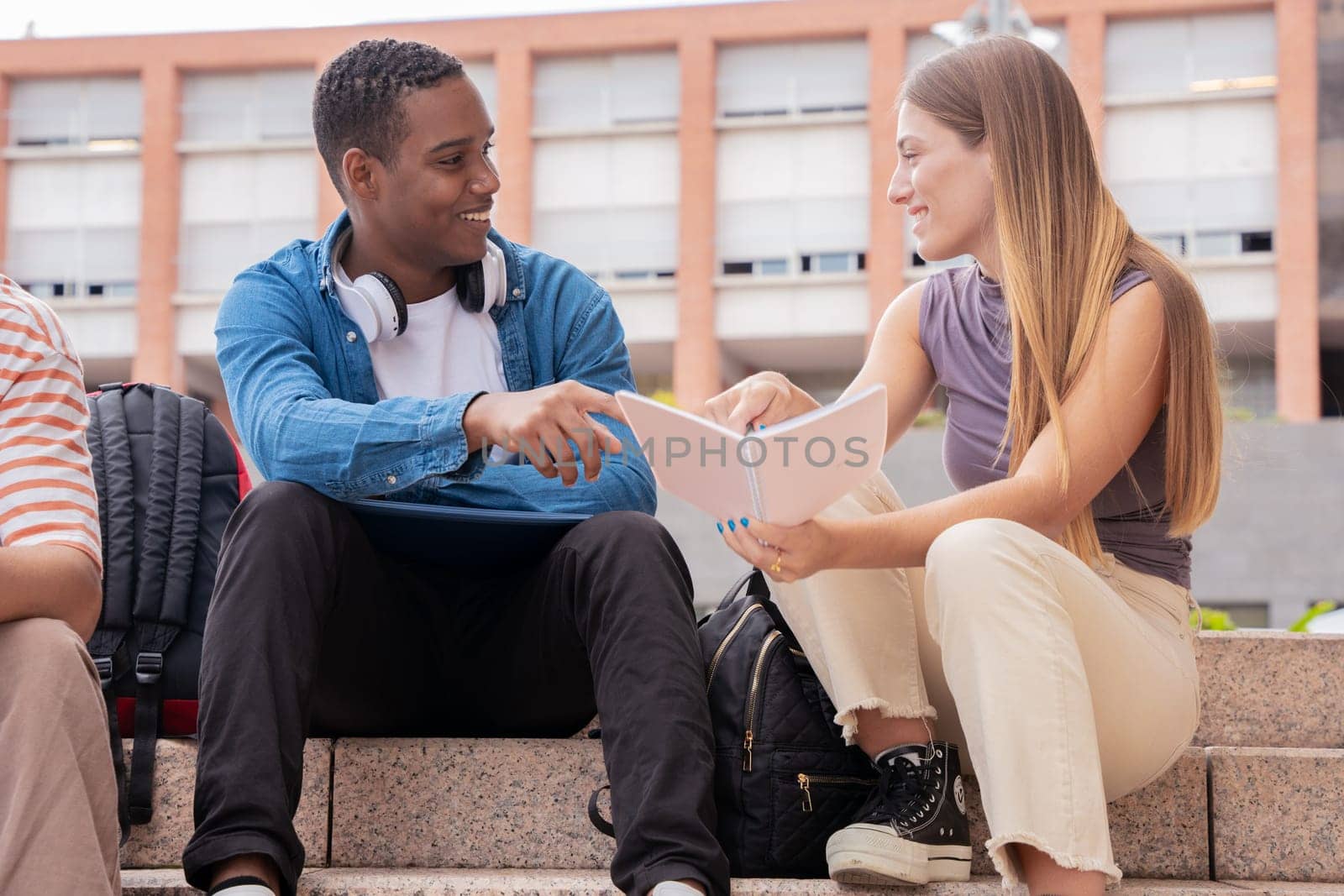 multiethnic smiling students sitting outdoors using a cell phone to chat online. University life concept