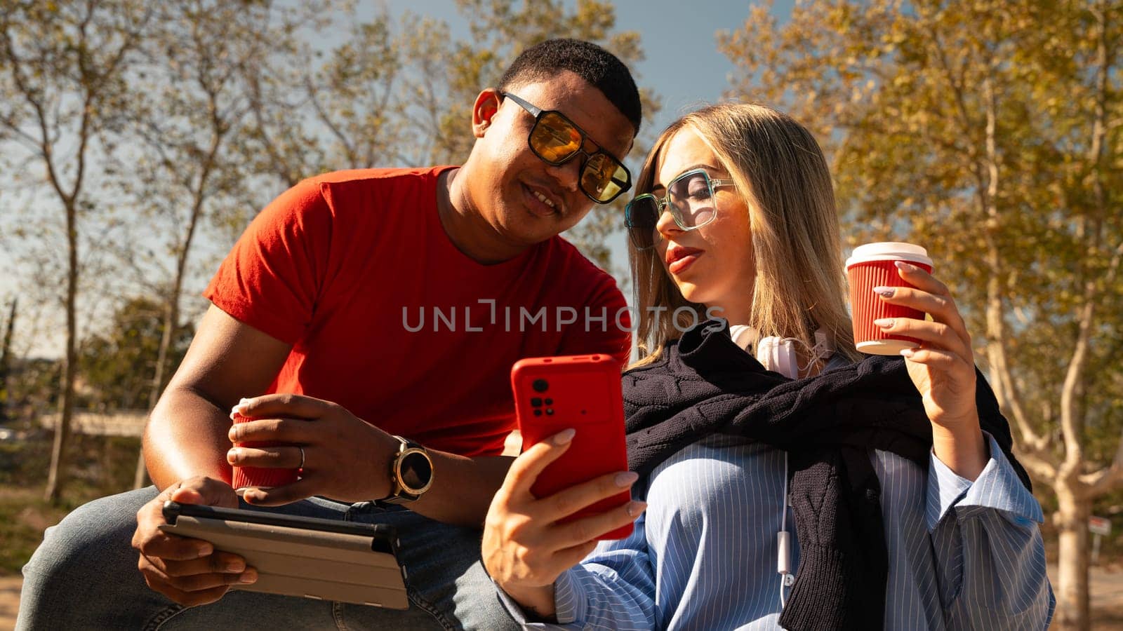 Happy multiracial couple in sunglasses making selfie on cell phone having fun an afternoon together in the park.