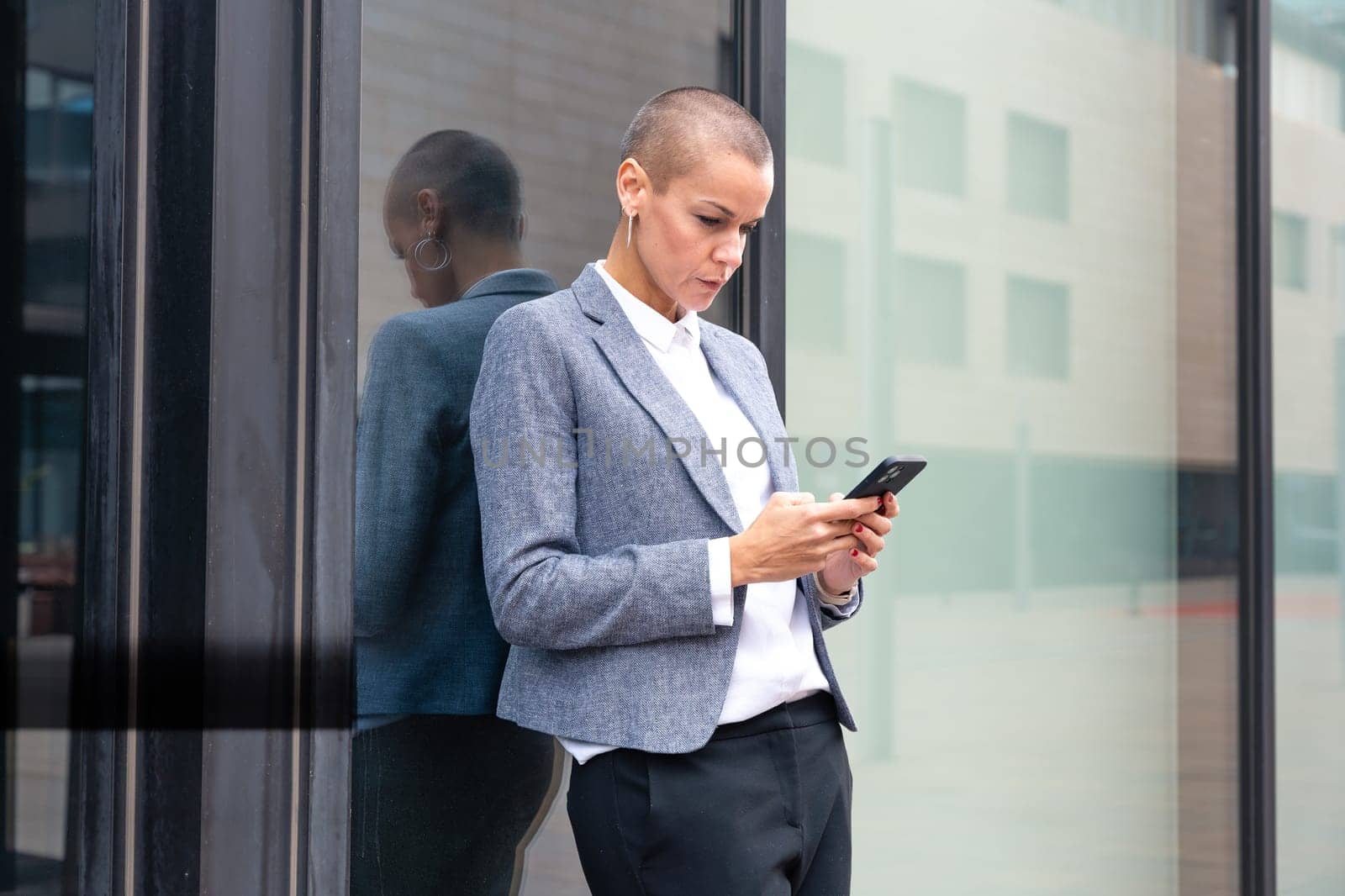 Satisfied with the results, the businesswoman walking on the street outside the office building, a mature boss holds a phone in her hands, writes messages and reads news online, using an app.