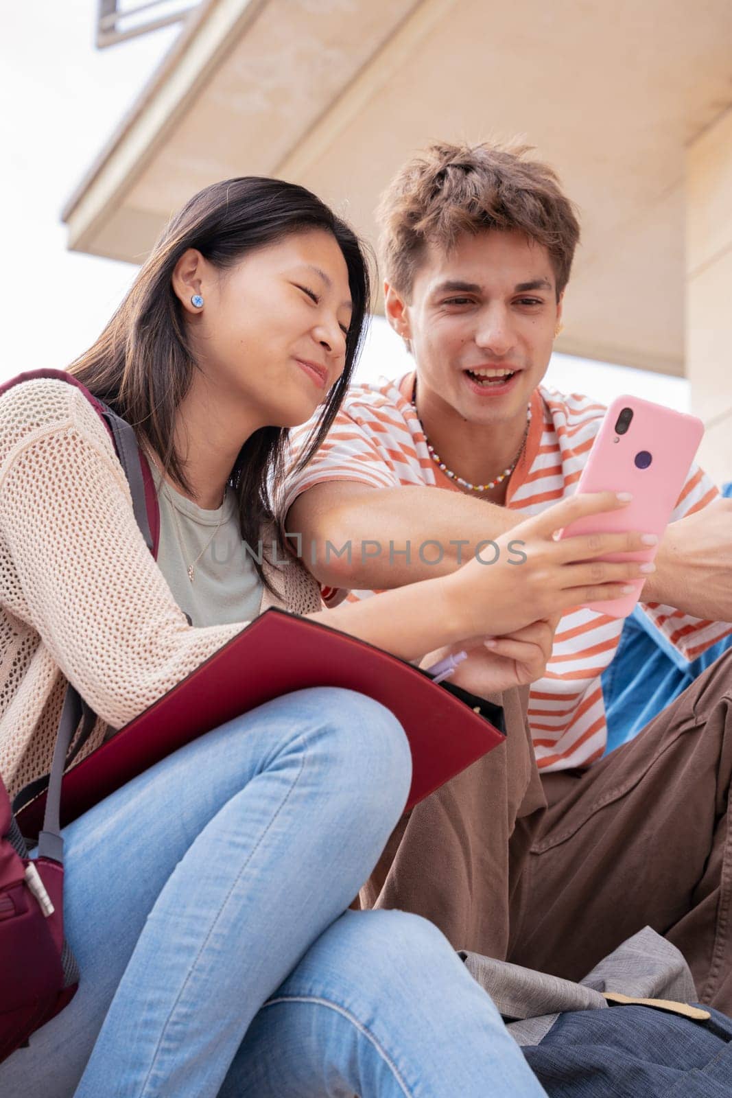 smiling multiracial students sitting outdoors using cell phone to chat online. University life concept