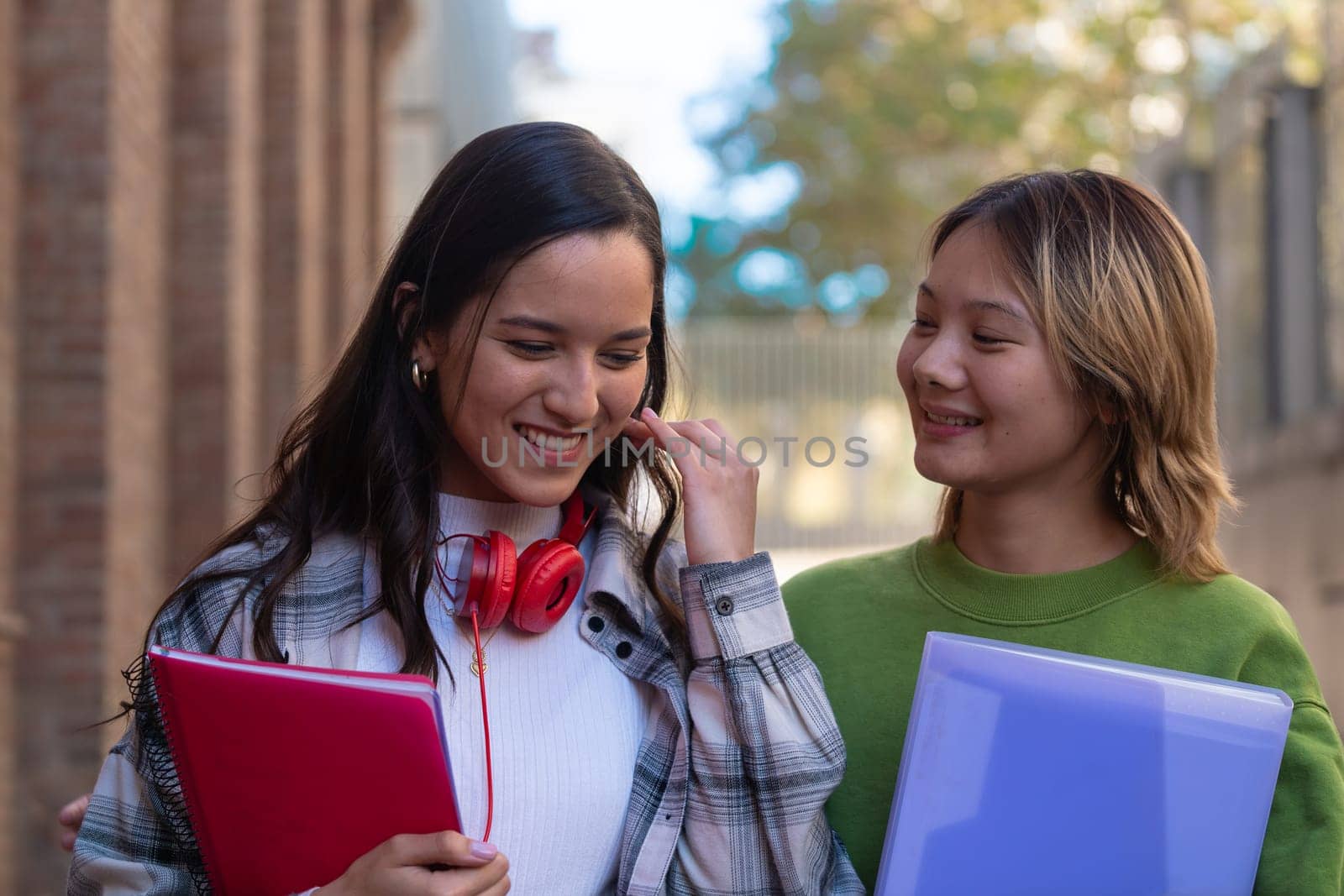 Happy young college girls talking and laughing as they walk around campus. Asian and Latin American Youth