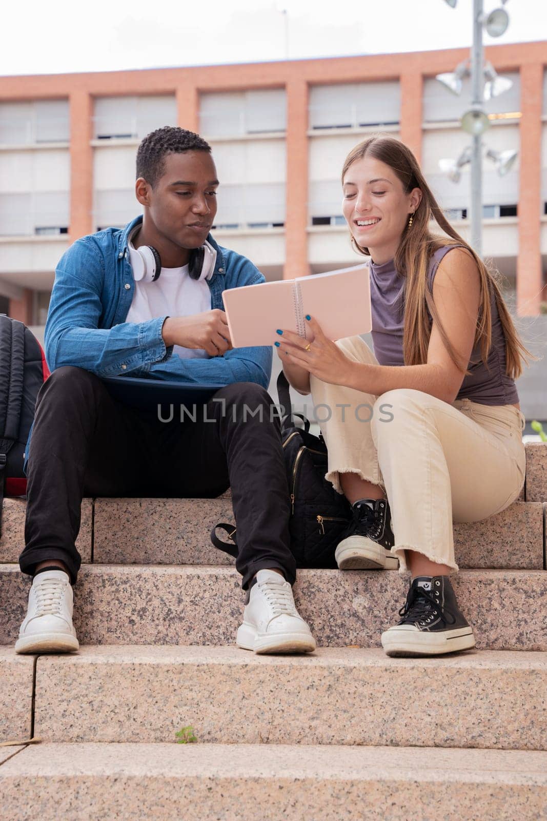 smiling multiracial college students sitting outdoors preparing for exam.