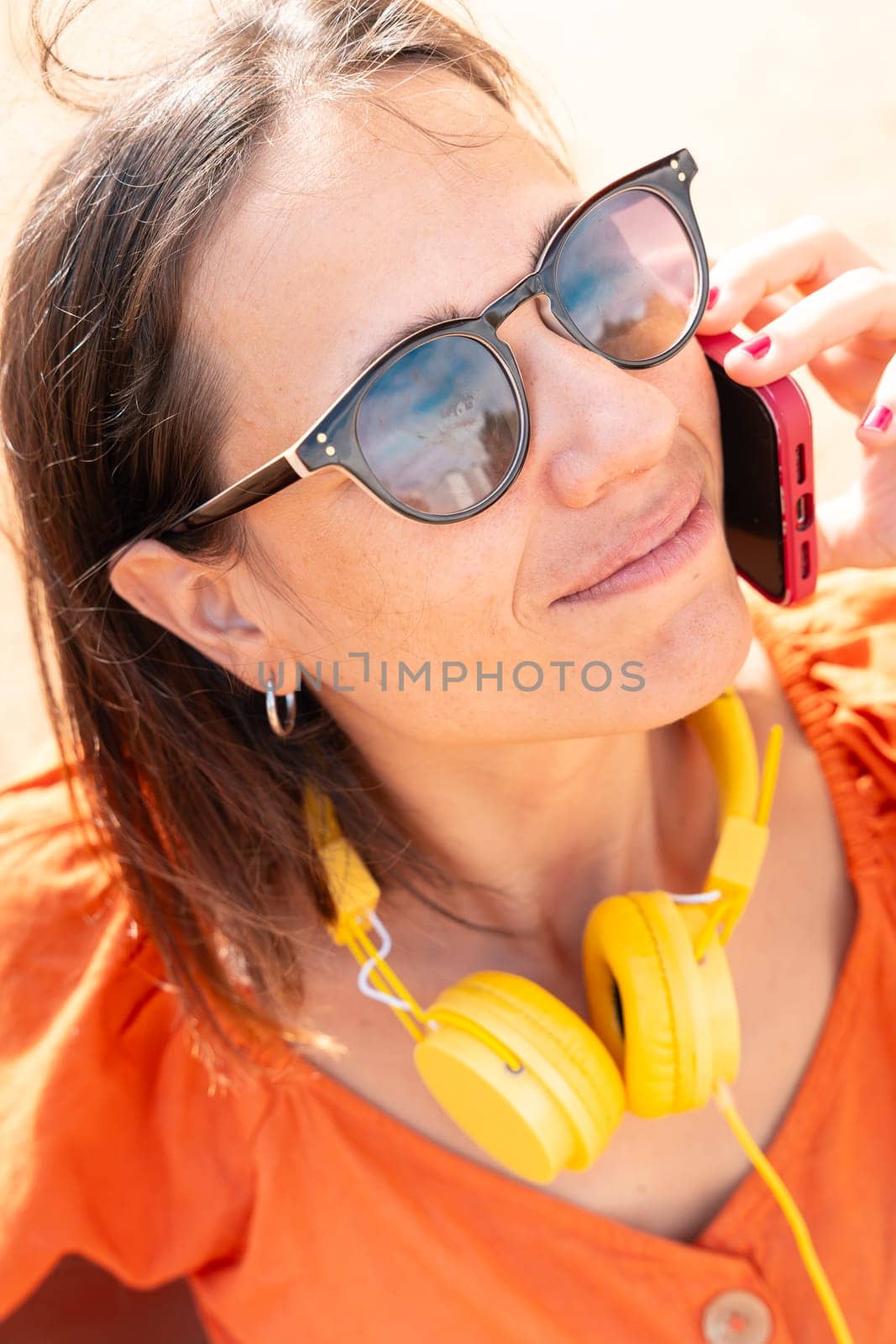 Close-up Beautiful young caucasian woman with headphones and sunglasses, having a conversation on cell phone.