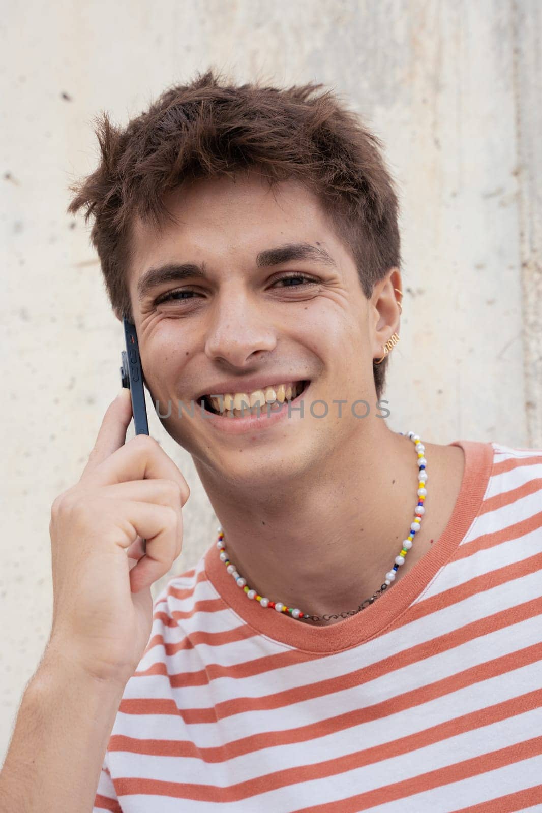 Beautiful caucasian teenage student smiling and talking on mobile phone outdoors. Boy talking on mobile phone
