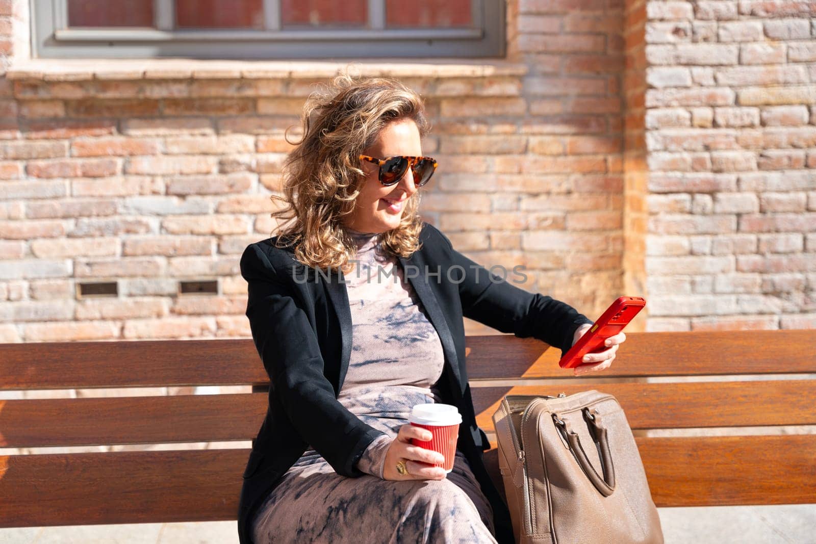 Woman wearing sunglasses with cell phone in hands, writes messages and reads news online, using an app.