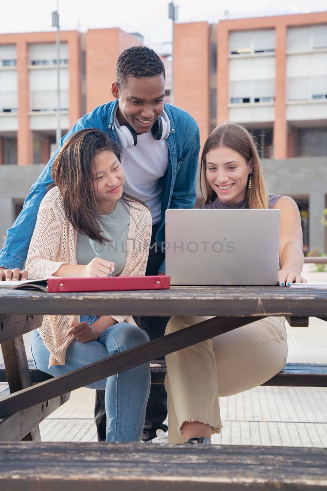 Vertical photo A group of three students with laptops and notes sit near the campus to review the exam.