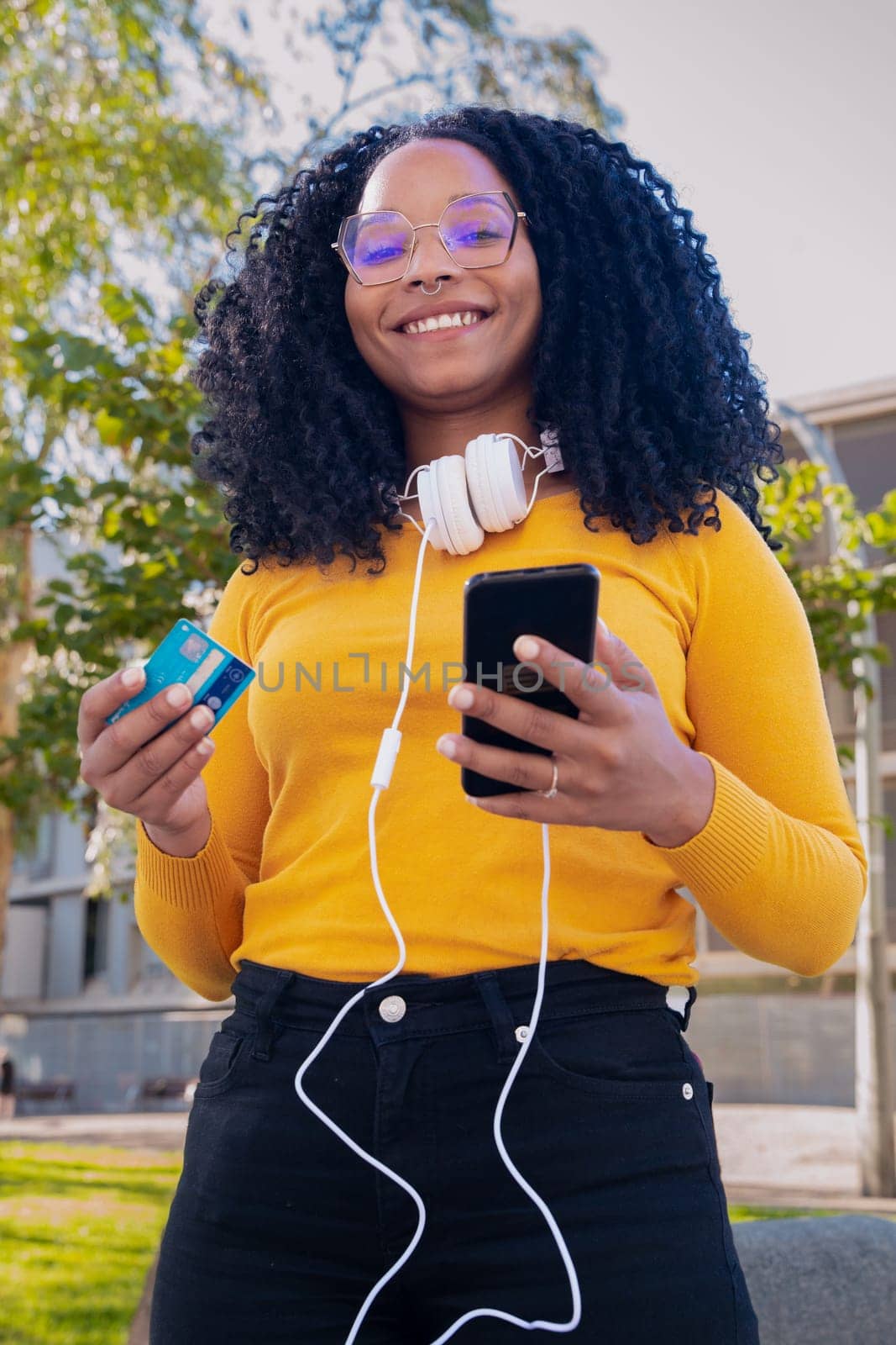 vertical photo happy black woman with credit card and smartphone in hands. Looking at camera. Concept: online store payment
