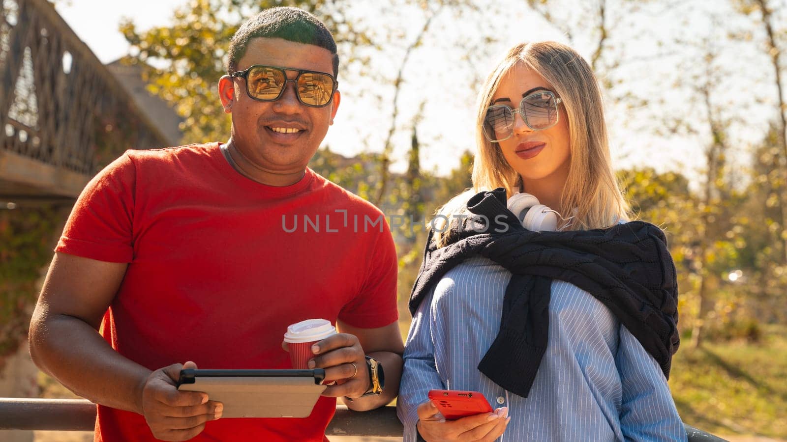 Cute multiethnic couple of man and woman standing browsing smartphone apps shopping online looking at camera