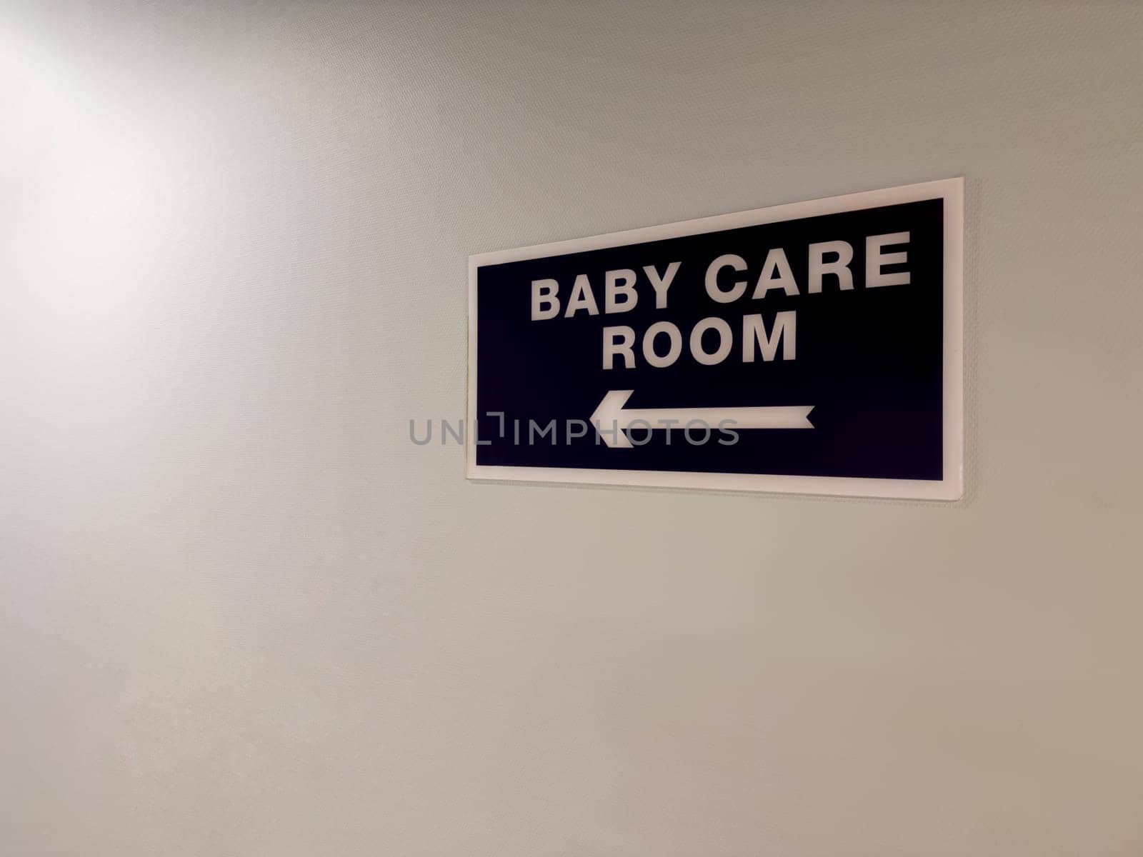 Sign on wall of corridor with directional arrow towards baby care room. Special room for parents to change the baby diaper. Important room when building infrastructure in public place