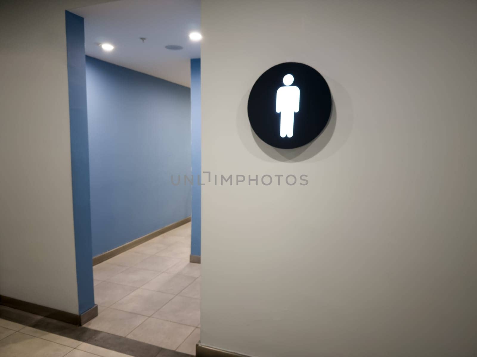 Sign on wall indicating men restroom in building. Man using public toilet. Entrance to room to relieve man needs in public place. Entrance to toilet with separation of people by gender