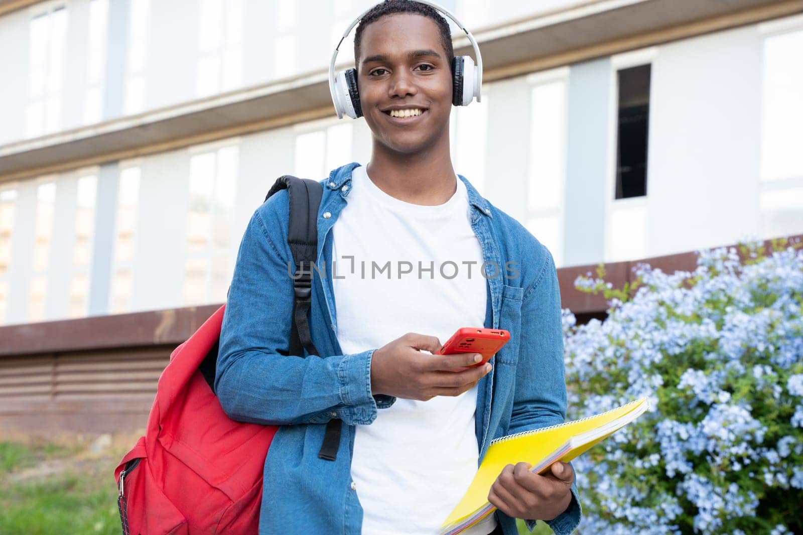 A happy student with headphones and folder is inside the university campus using a social media application. College life