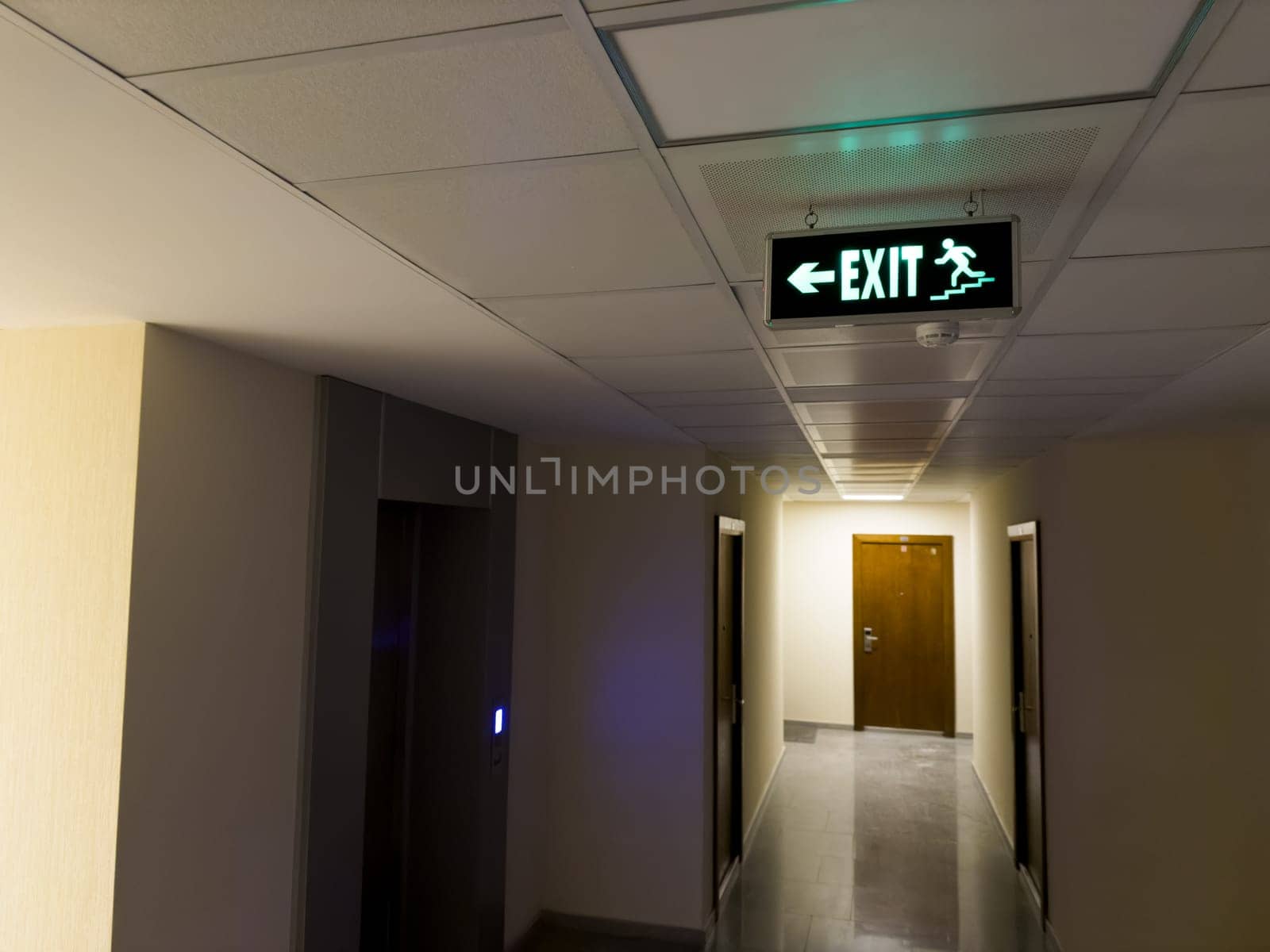 Sign on ceiling showing direction to emergency exits along stairs from burning building. Leaving building using emergency exits in case of emergency. Emergency exits from building with green sign