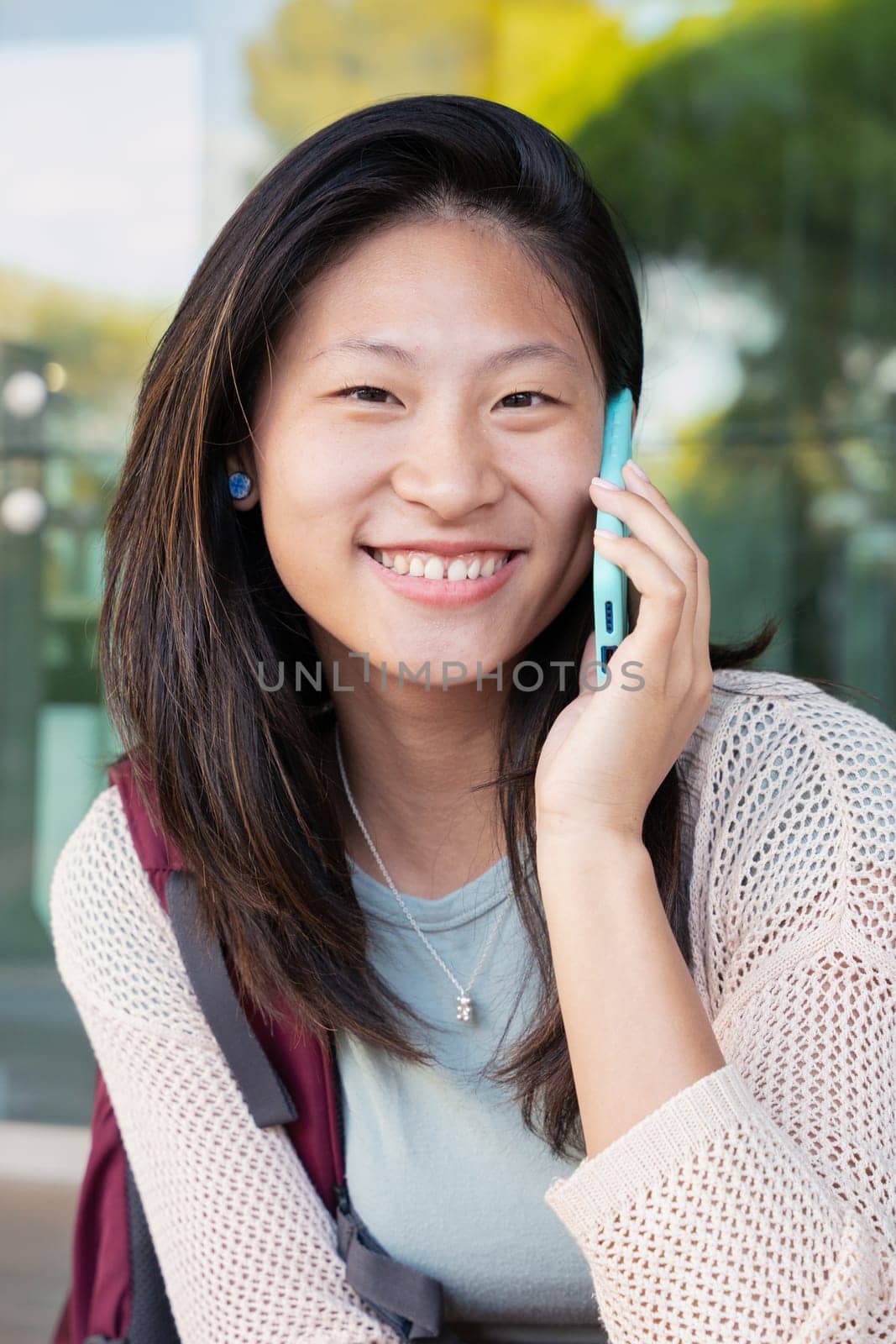 Close-up Beautiful Chinese teenage student smiling and talking on mobile phone outdoors. Girl talking on mobile phone