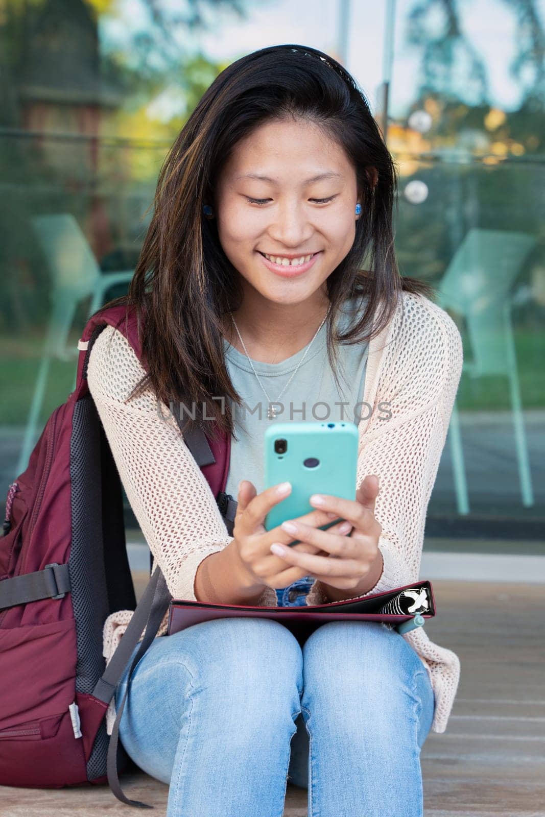 Beautiful Chinese teenage student smiling using social media app on tablet outdoors. Girl chatting on mobile phone