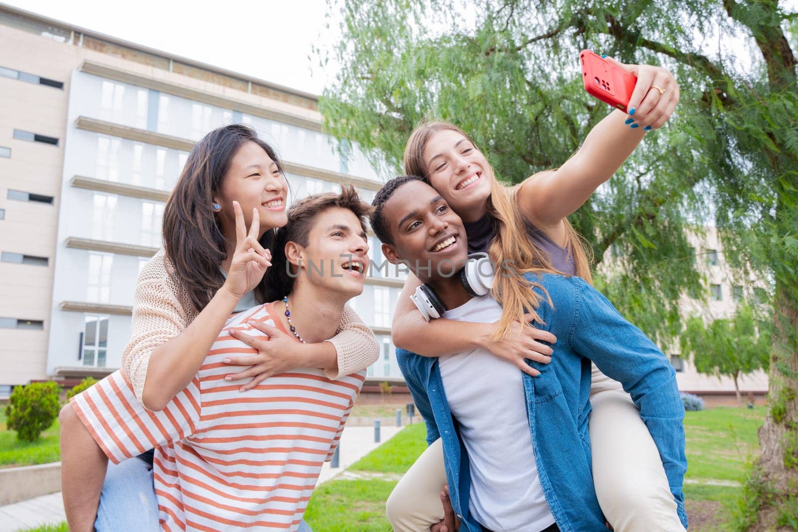 Young students piggybacking their fellow college students on campus. Excited friends posing for a funny photo.