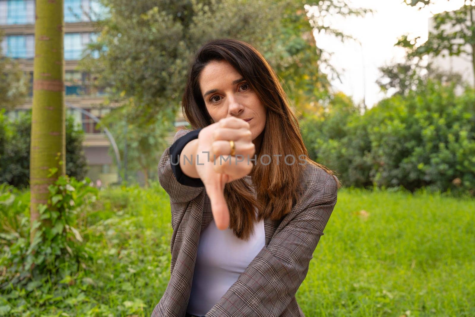 Close-up of a happy young Caucasian woman pointing with her thumbs down. Angry facial expression.
