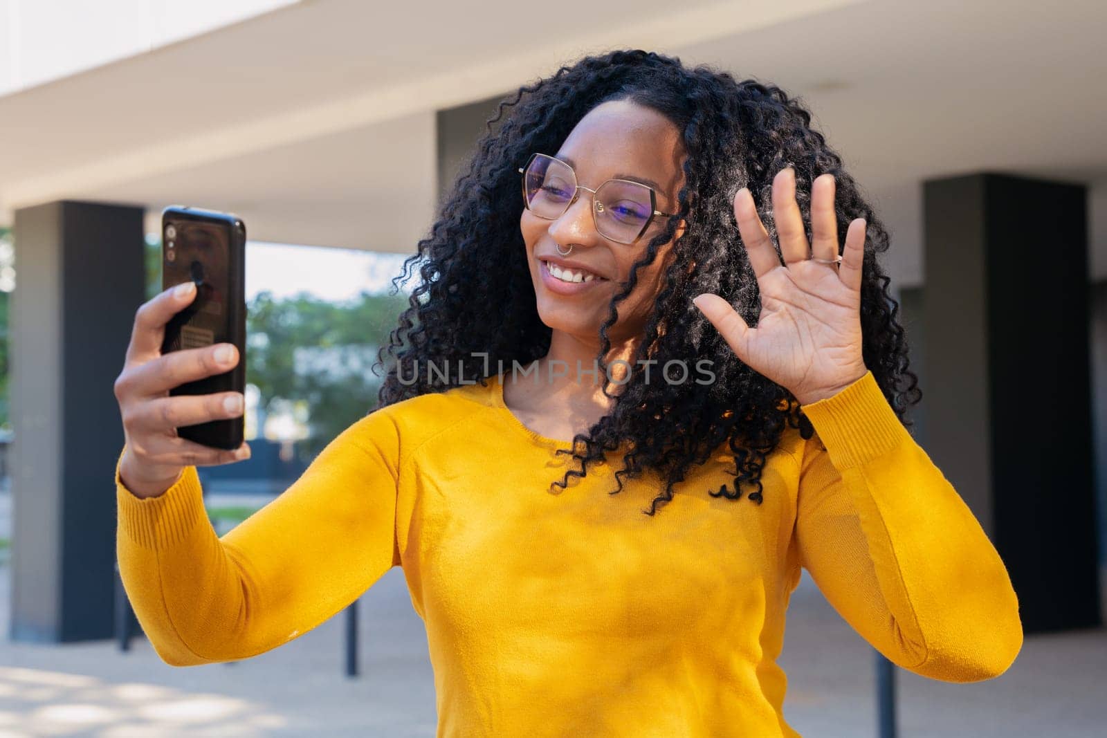 smiling young african american woman looking at camera having a video conference with her smartphone outdoors.