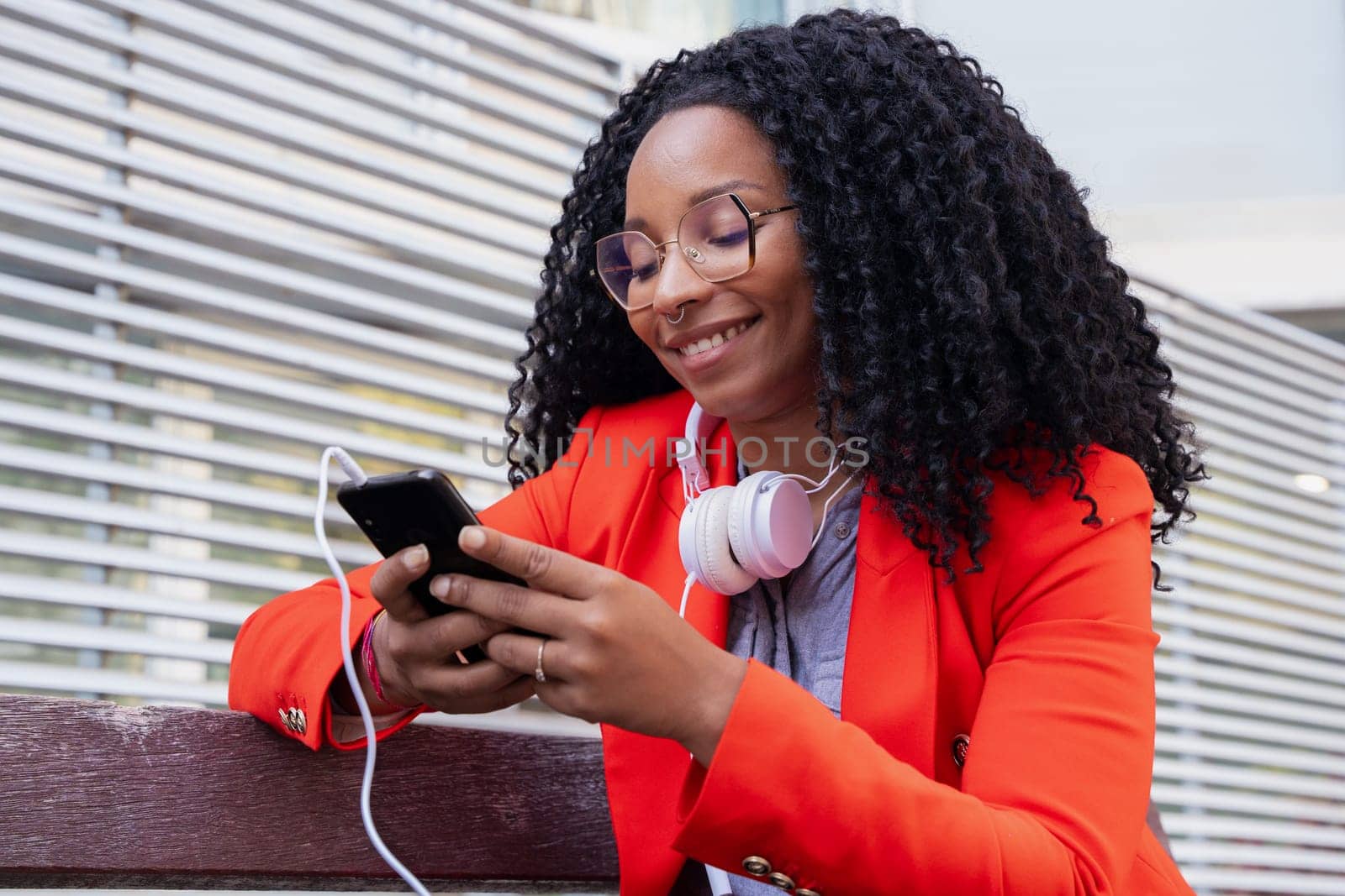 Beautiful black woman in glasses smiling using a social media app on a mobile phone outdoors. Girl chatting on mobile phone.Girl chatting on mobile phone.