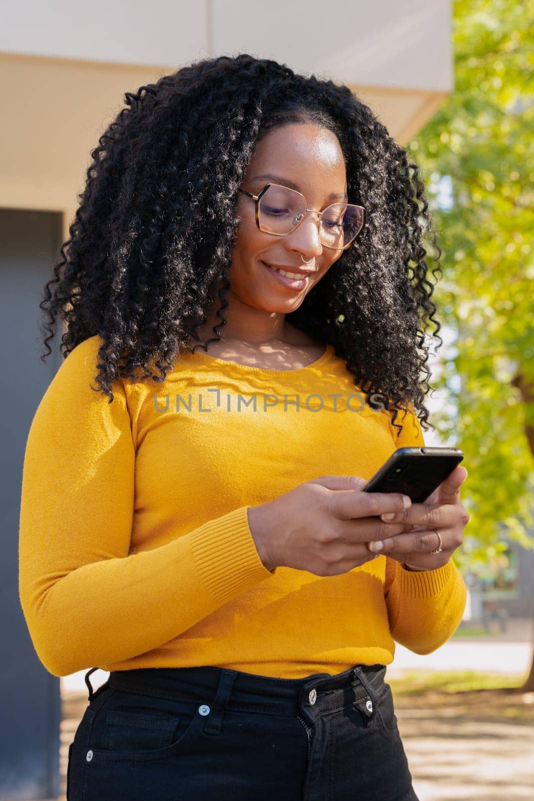 Beautiful black woman with curly hair using her smartphone to chat with friends. connected concept