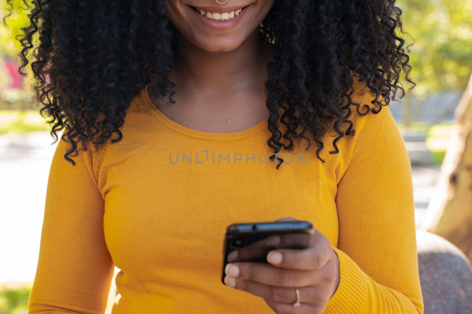 close-up of a beautiful black woman smiling while holding, using and looking at a smartphone with a feeling of happiness