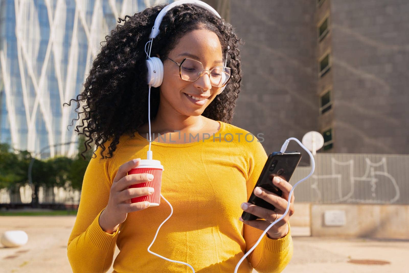 Happy teenager with headphones,drinking coffee sending messages using a cell phone outdoors. Communication