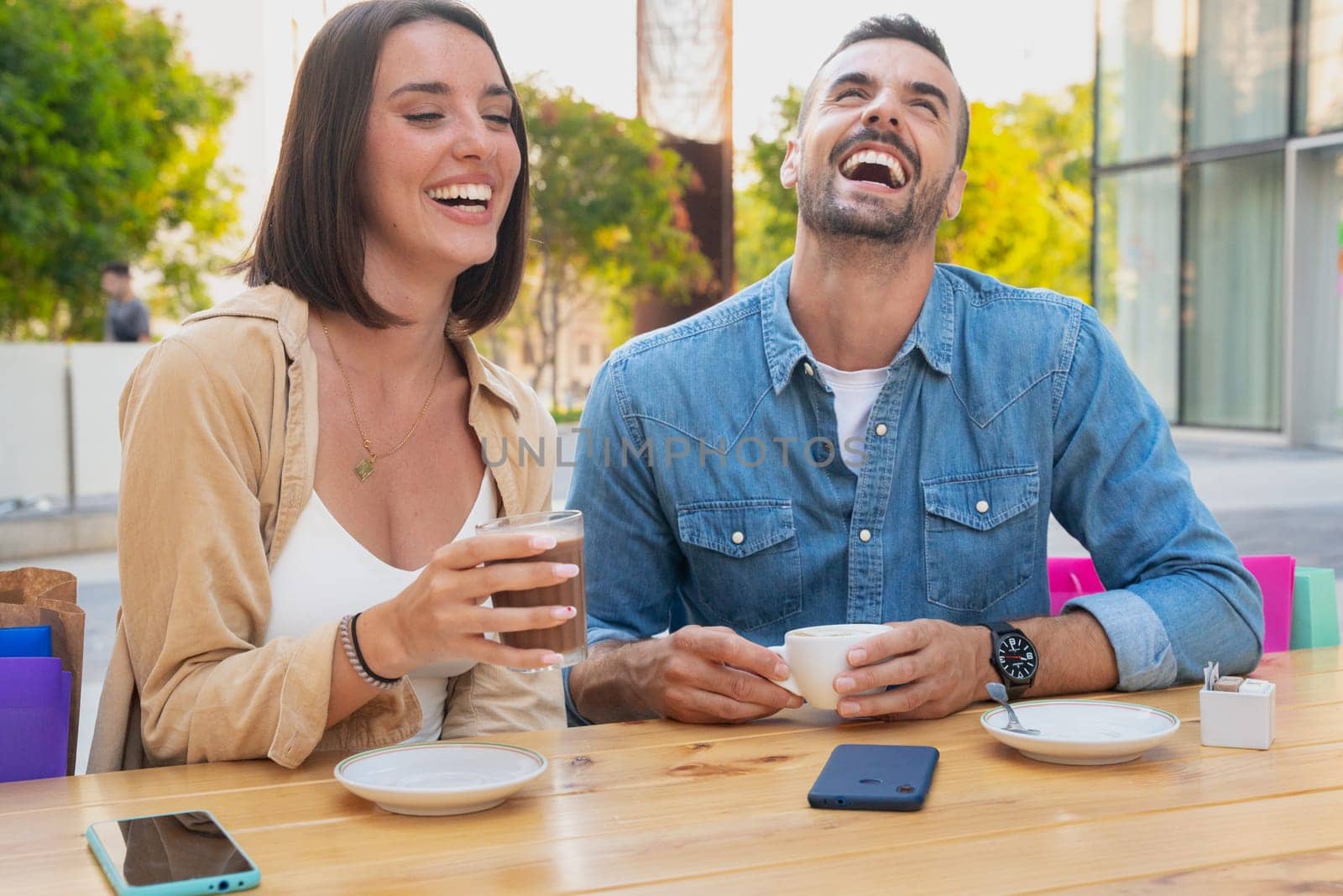 Two young friends chatting on a cafeteria terrace drinking coffee, laughing and having a good time after work.