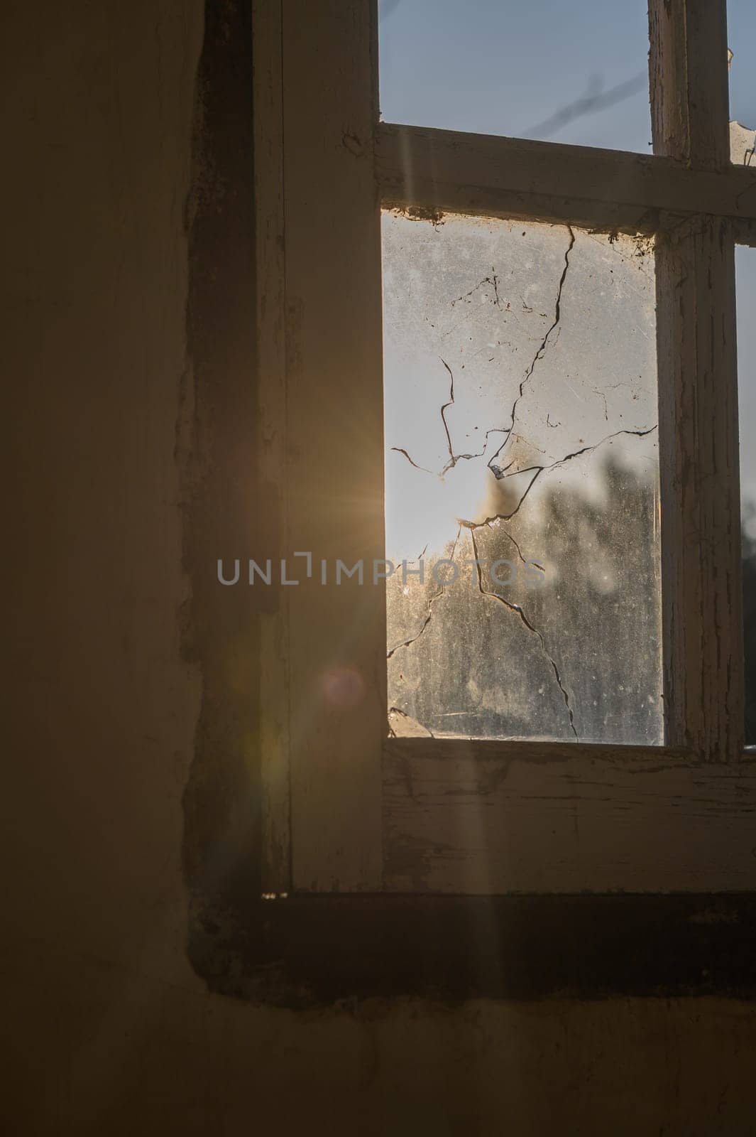 Soft rays of sunlight stream through a shattered window, illuminating dust particles dancing in the air.