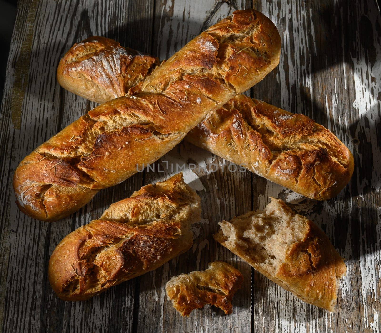 Golden crusted loaves of artisan bread sit on a weathered wooden surface, highlighting their texture and warmth.