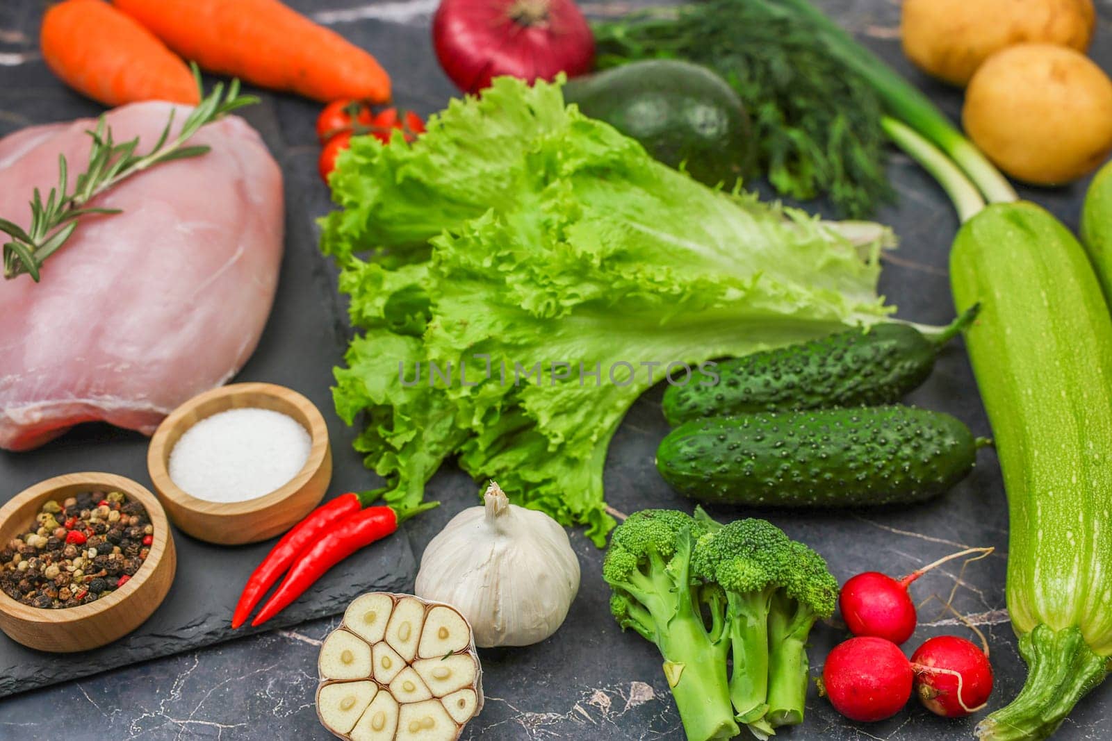 The concept of diet, detox, proper and healthy nutrition, recipes. Top view of raw turkey fillet with a sprig of rosemary lies on a black stone plank surrounded by vegetables, herbs, spices on a dark background. High quality photo
