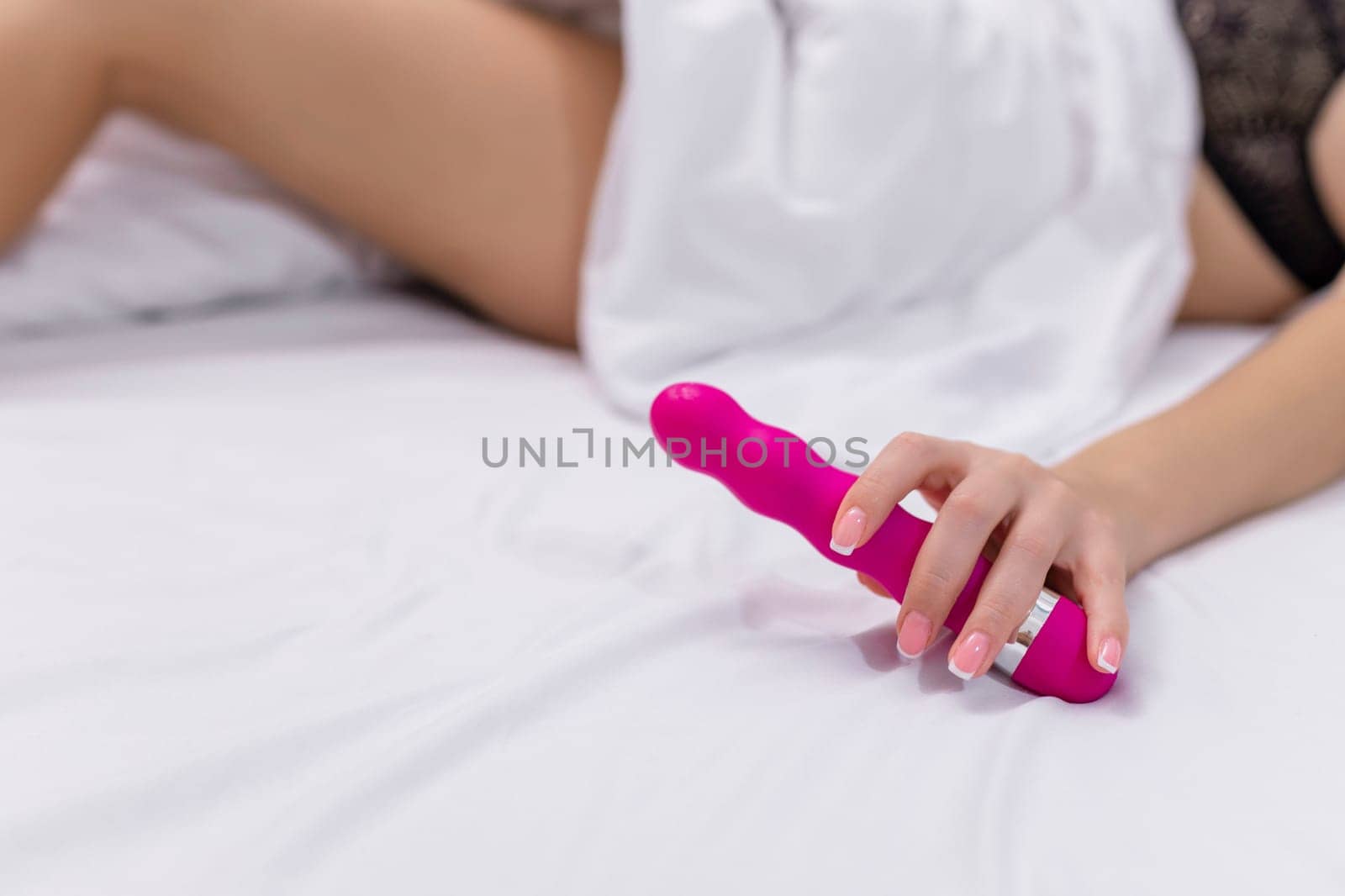 Young woman holding sex toy dildo vibrator in bed.