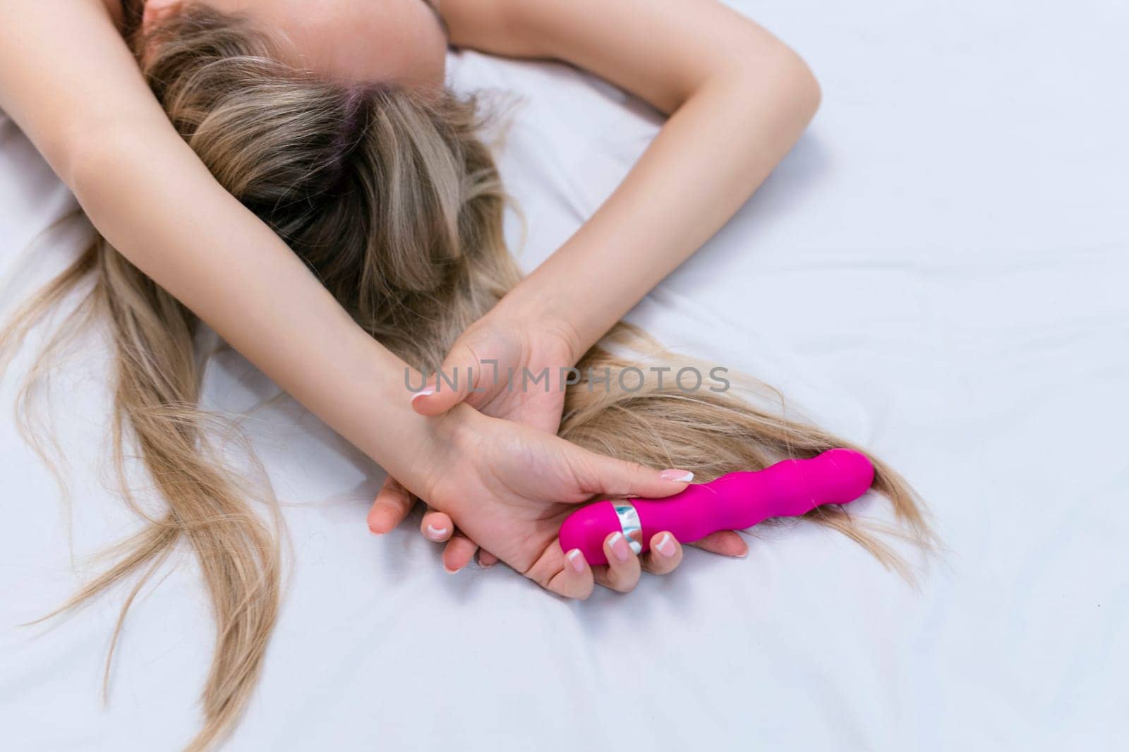 Woman in bed under sheets holding vibrator in hand. High quality photo