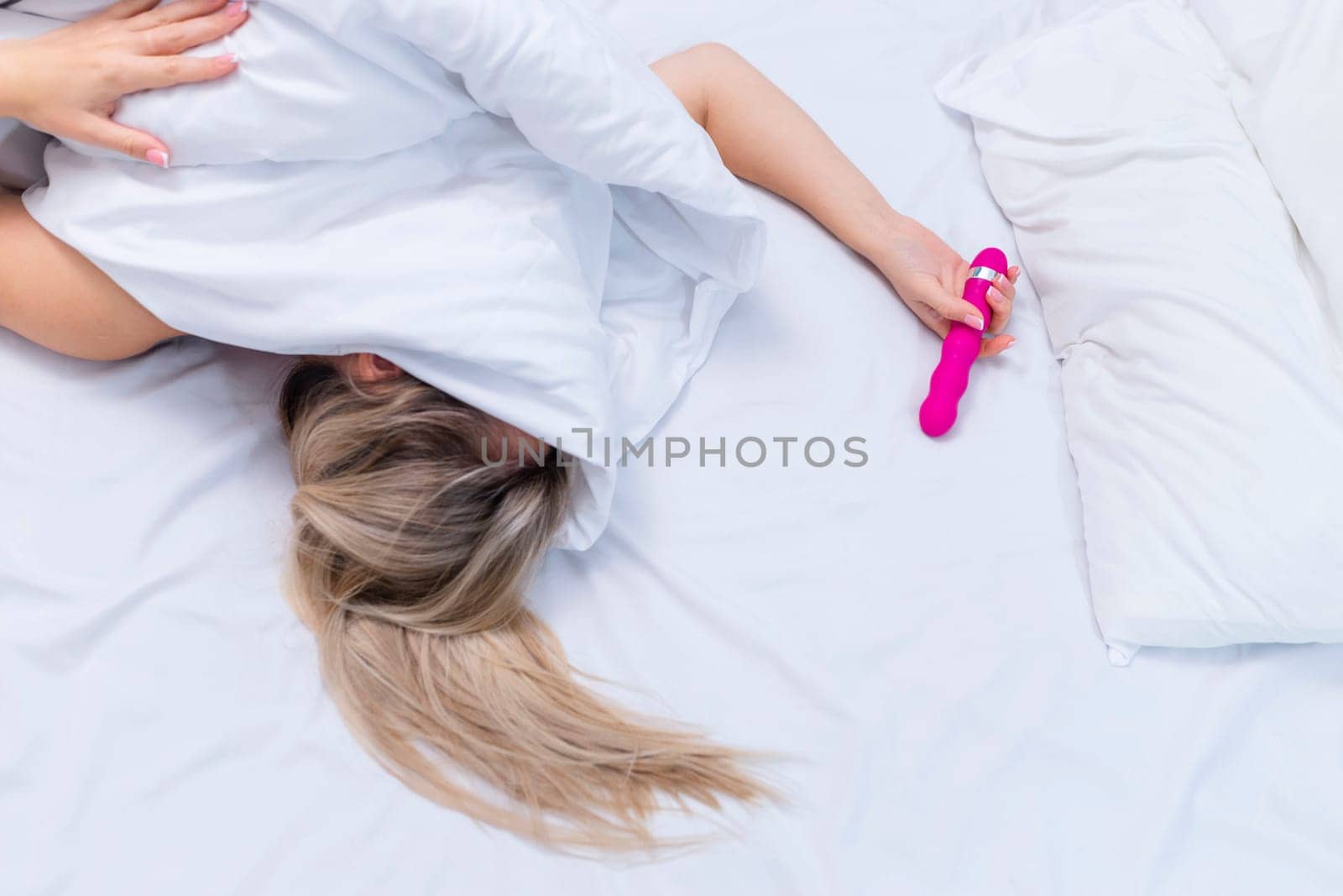 Woman in bed under sheets holding vibrator in hand. High quality photo