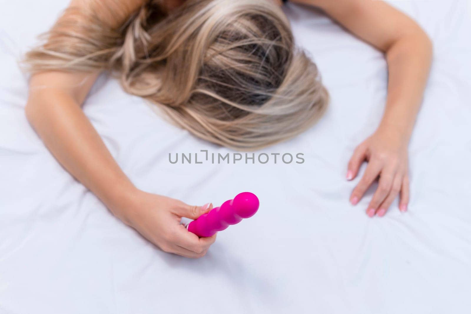 Woman in bed under sheets holding vibrator in hand. High quality photo