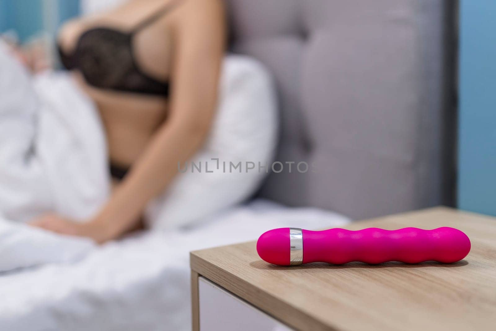 Young woman holding sex toy dildo vibrator in bed.