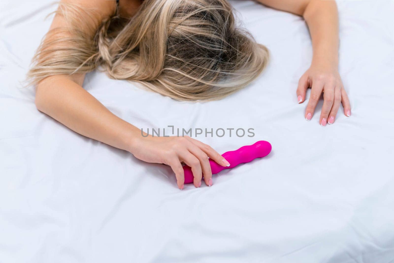 Woman in bed under sheets holding vibrator in hand. High quality photo