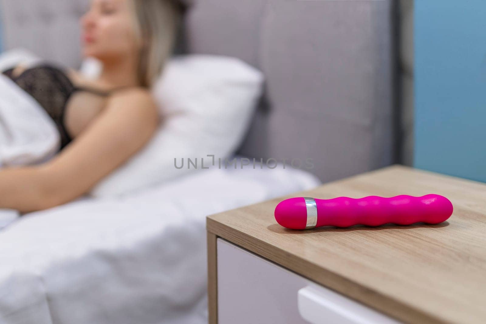Young woman holding sex toy dildo vibrator in bed.
